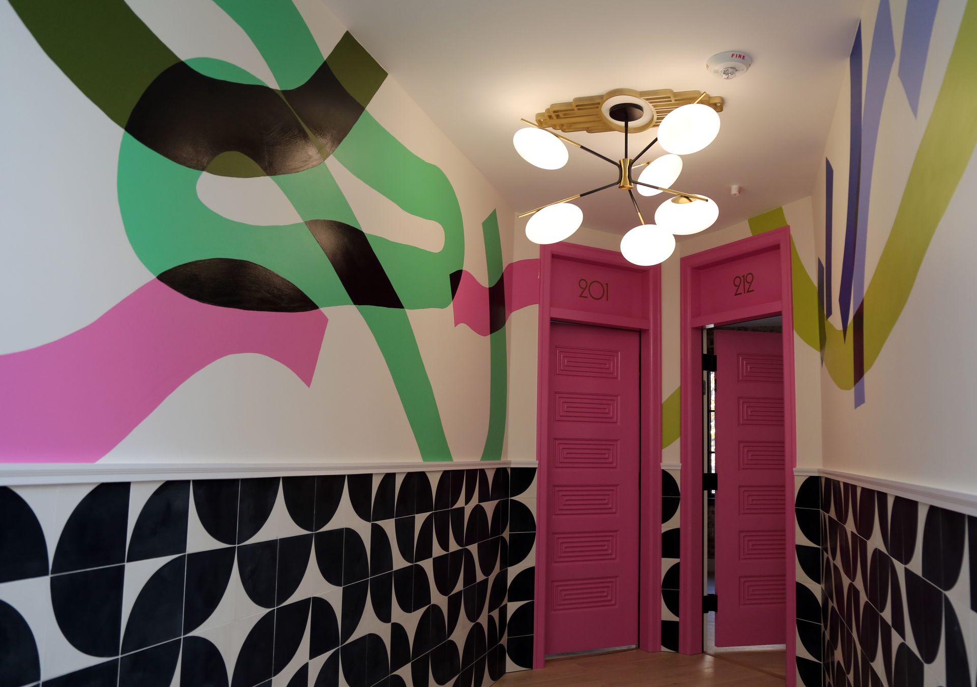 Colorful hallway with pink double doors, black patterned tile, and ceiling lights