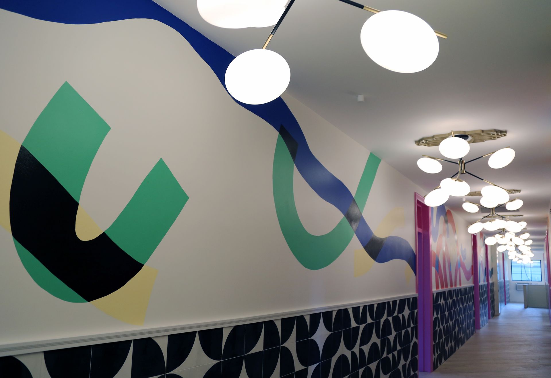 Colorful abstract wall mural in a modern hallway with round ceiling lights and patterned flooring