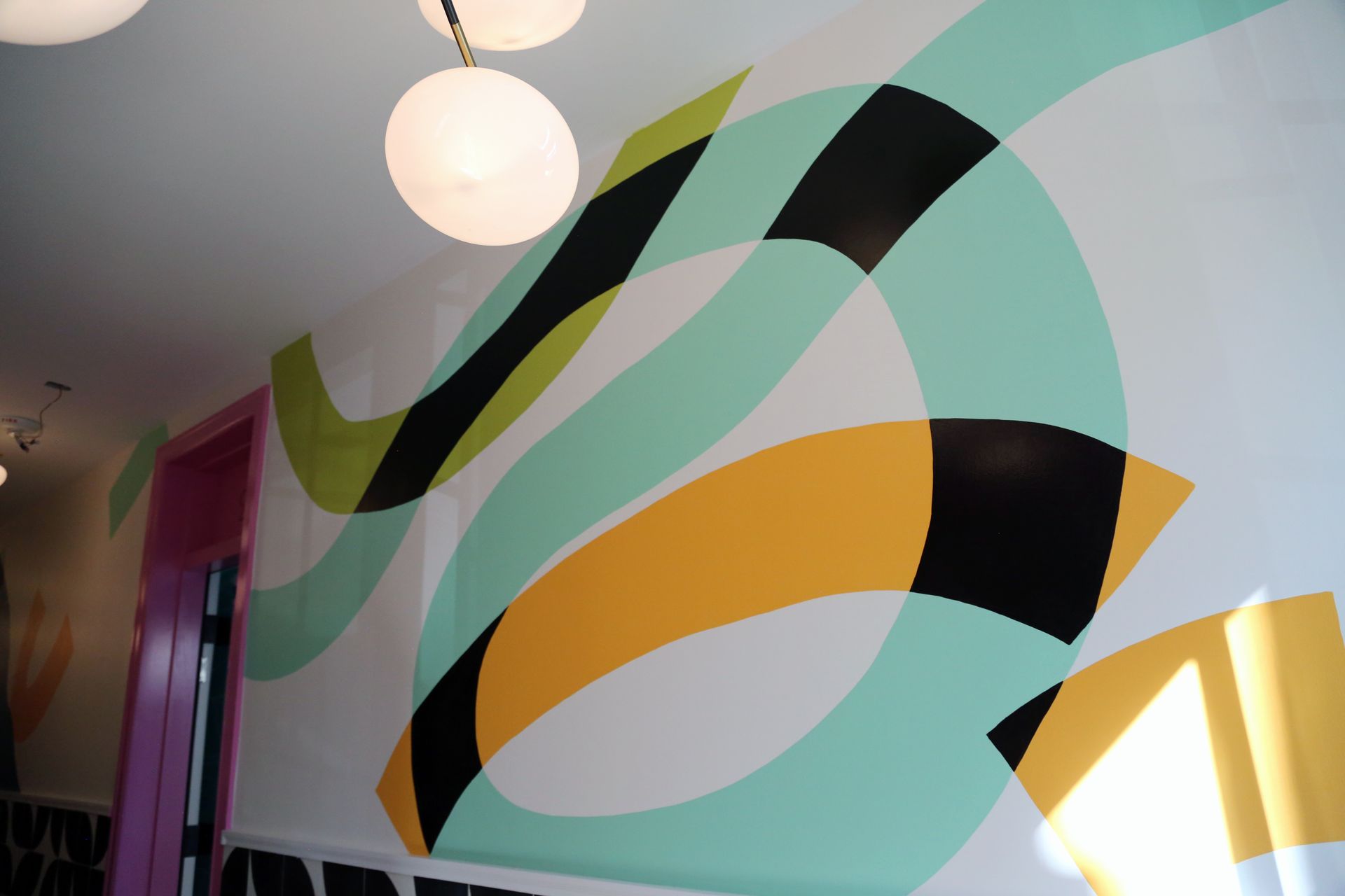 Abstract mural with sweeping teal, black, and gold shapes on a hallway wall under a round ceiling light