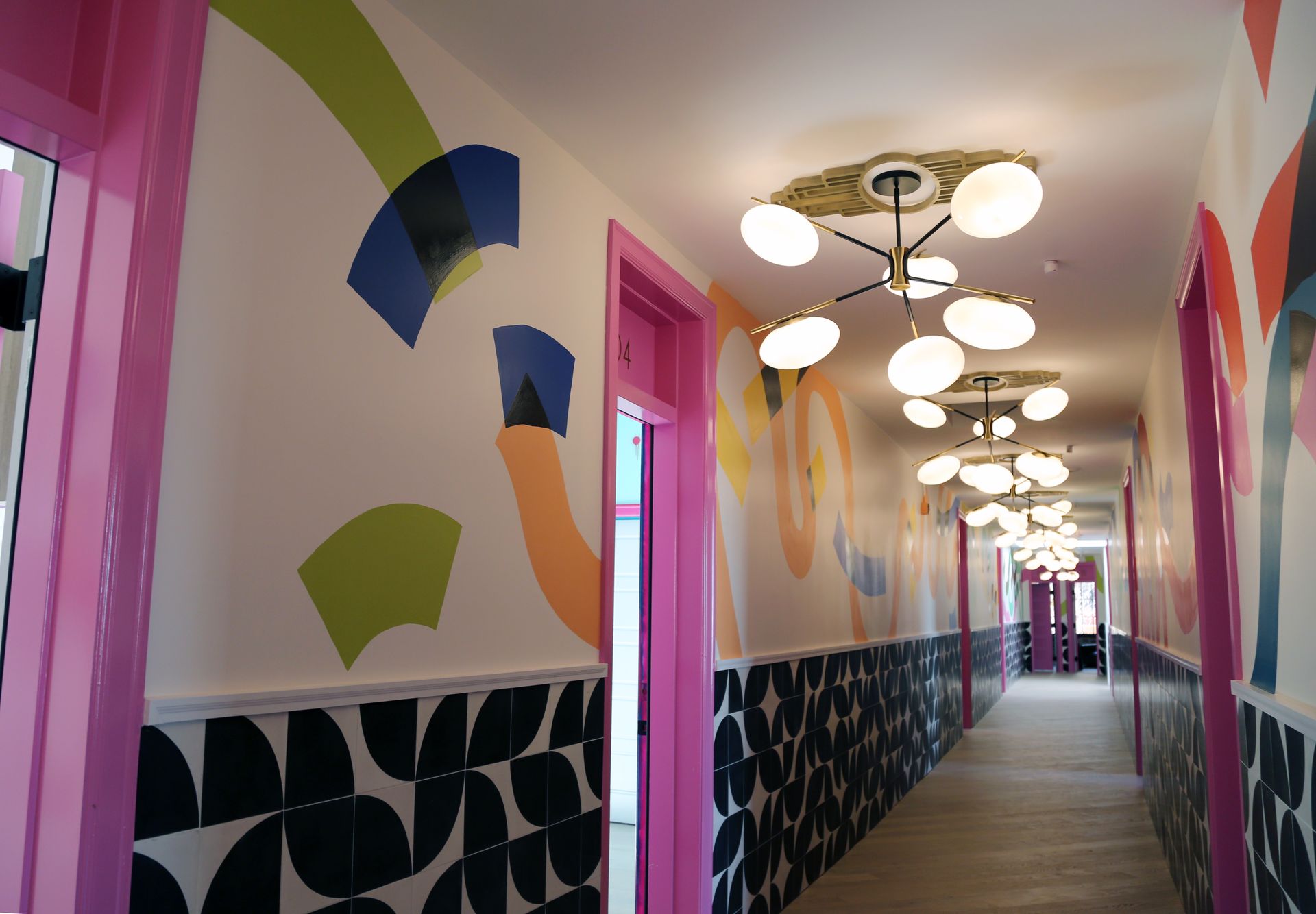 Bright hallway with colorful abstract wall art, pink doors, and hanging lights