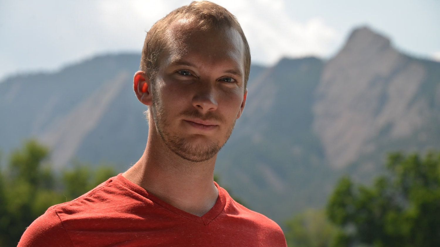 Person in a red shirt standing outdoors with mountains in the background