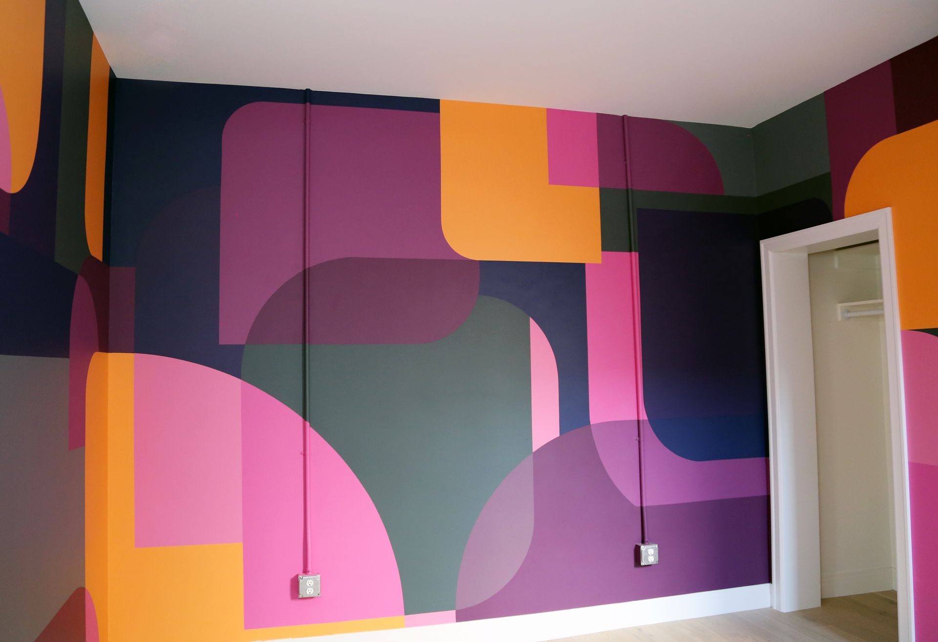 Colorful geometric mural in a room with pink, purple, orange, and black shapes on the walls.