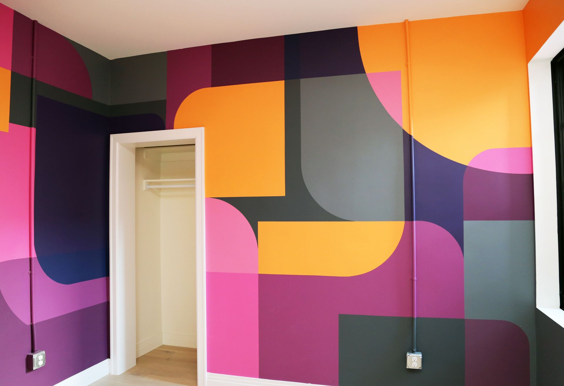 Colorful geometric mural on an interior wall with orange, pink, purple, and gray shapes near a doorway