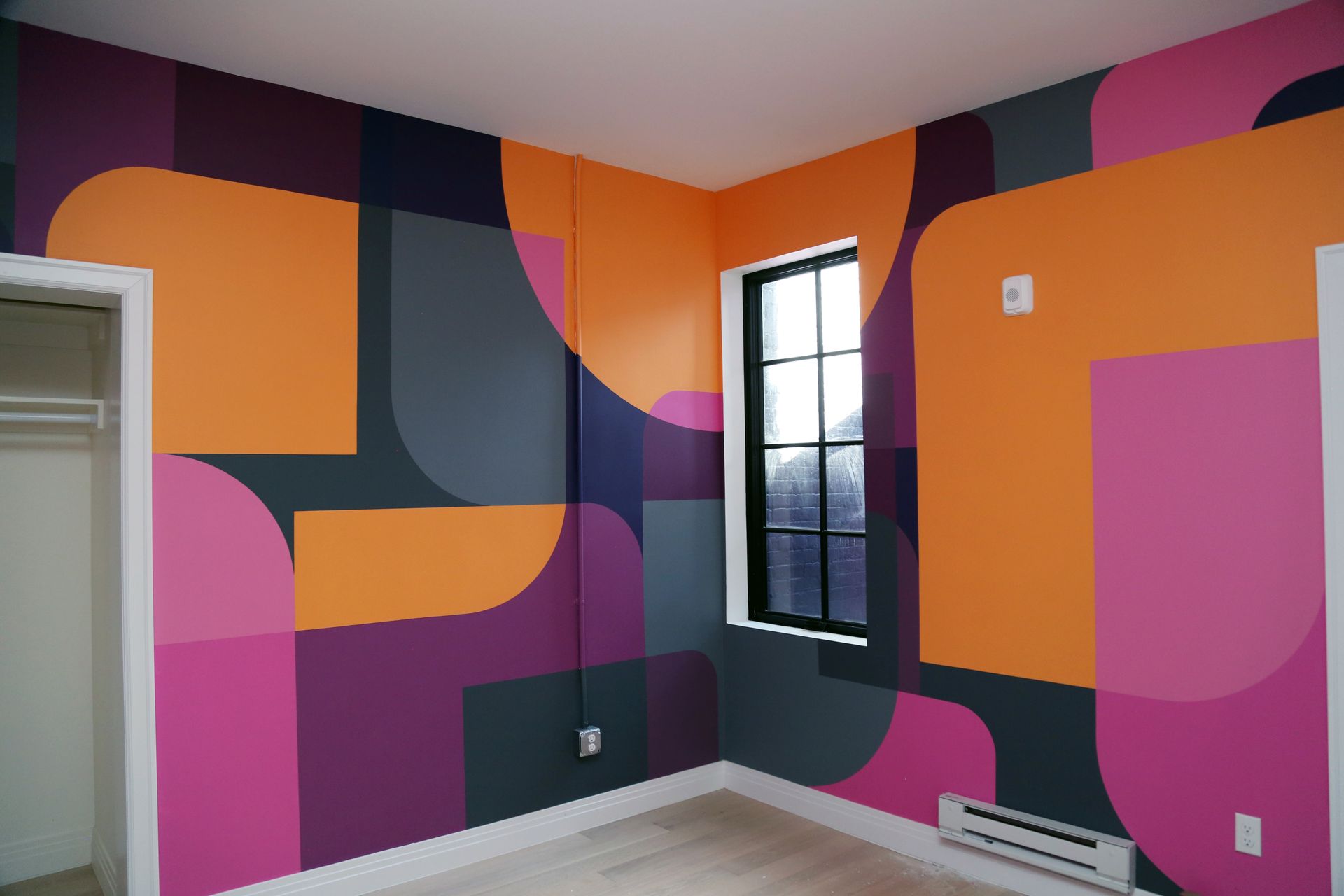 Colorful geometric mural painted on a small room's walls with orange, purple, pink, and dark gray shapes.