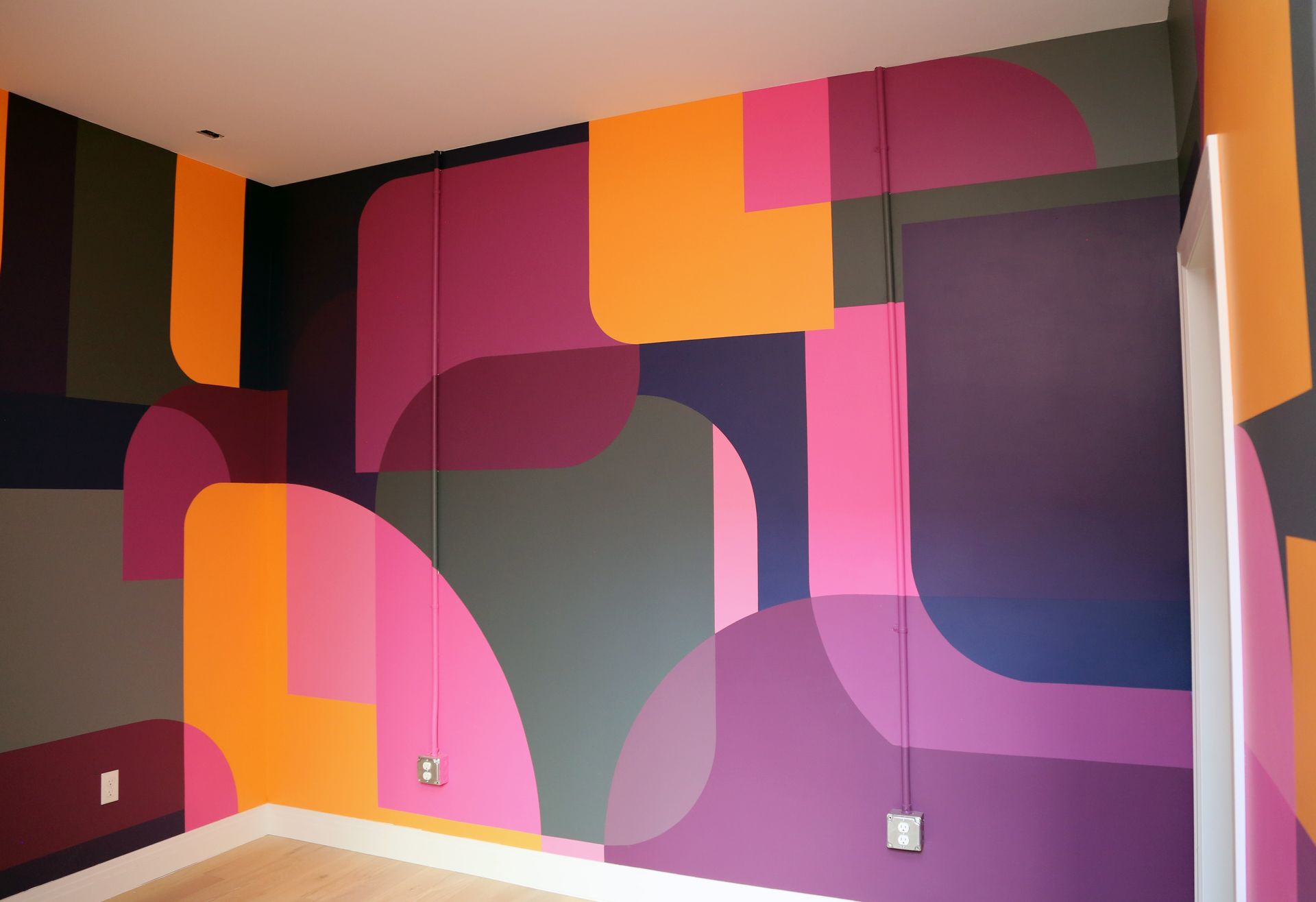 Abstract geometric mural in pink, purple, orange, and black on an indoor wall
