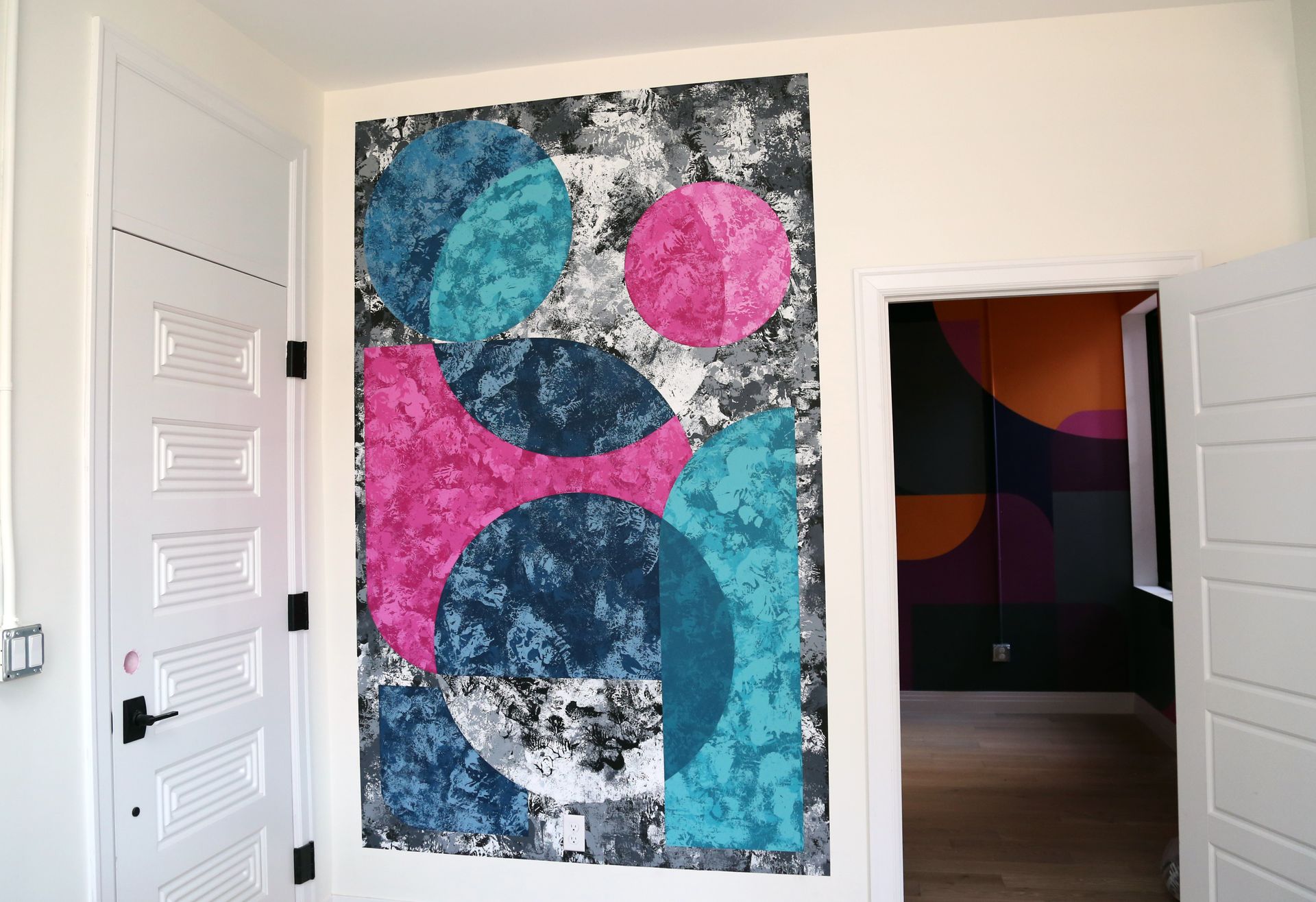 Abstract colorful painting on a white wall beside an open doorway to a dark room