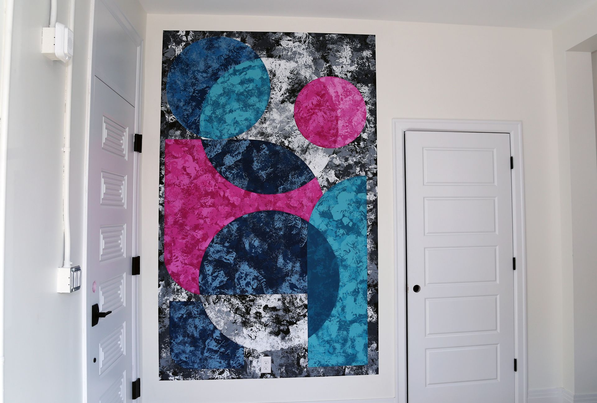 Abstract colorful geometric wall art with blue, pink, white, and black shapes in a room above a doorway
