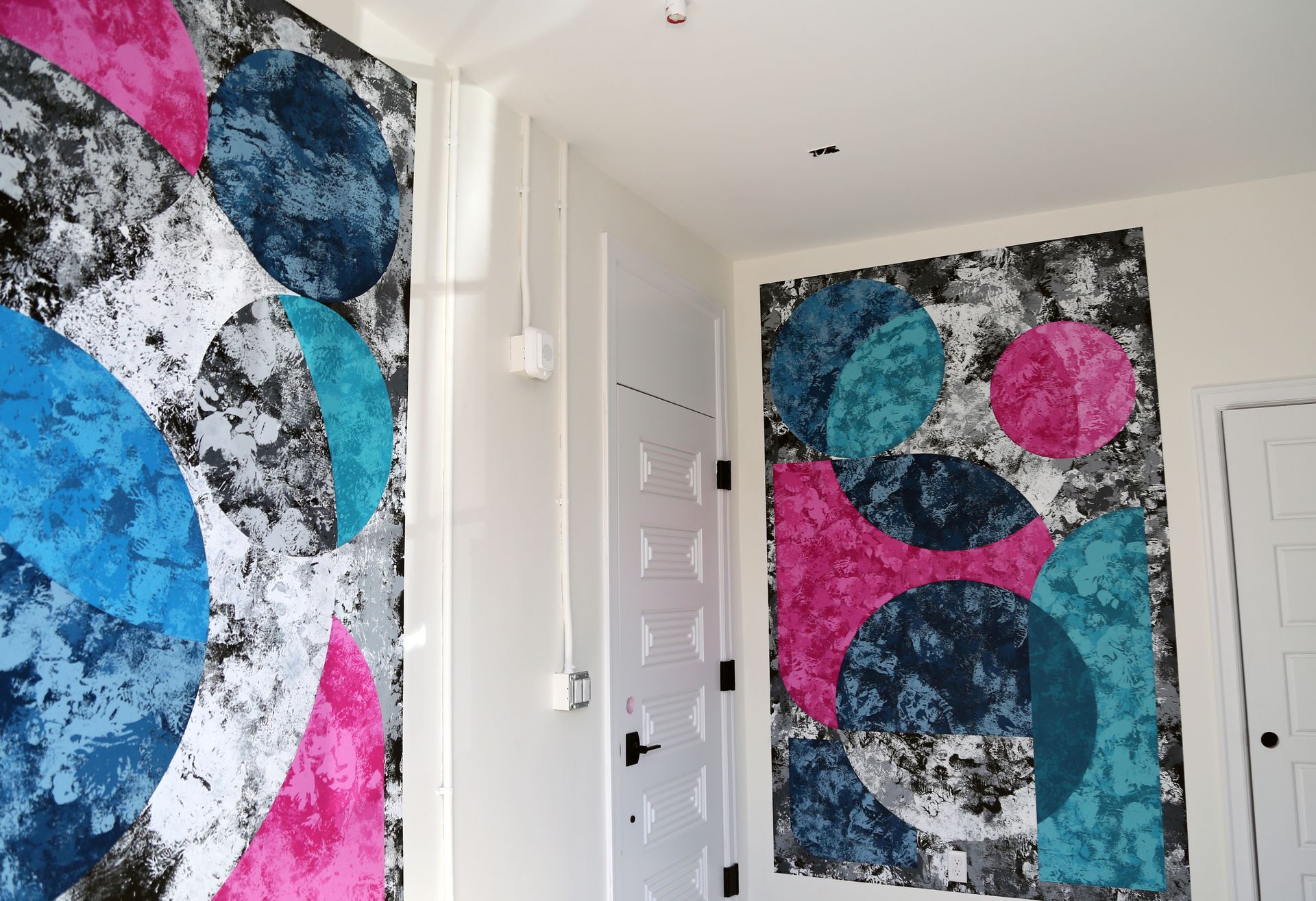 Bright hallway with two colorful abstract wall murals in blue, pink, black, and white.