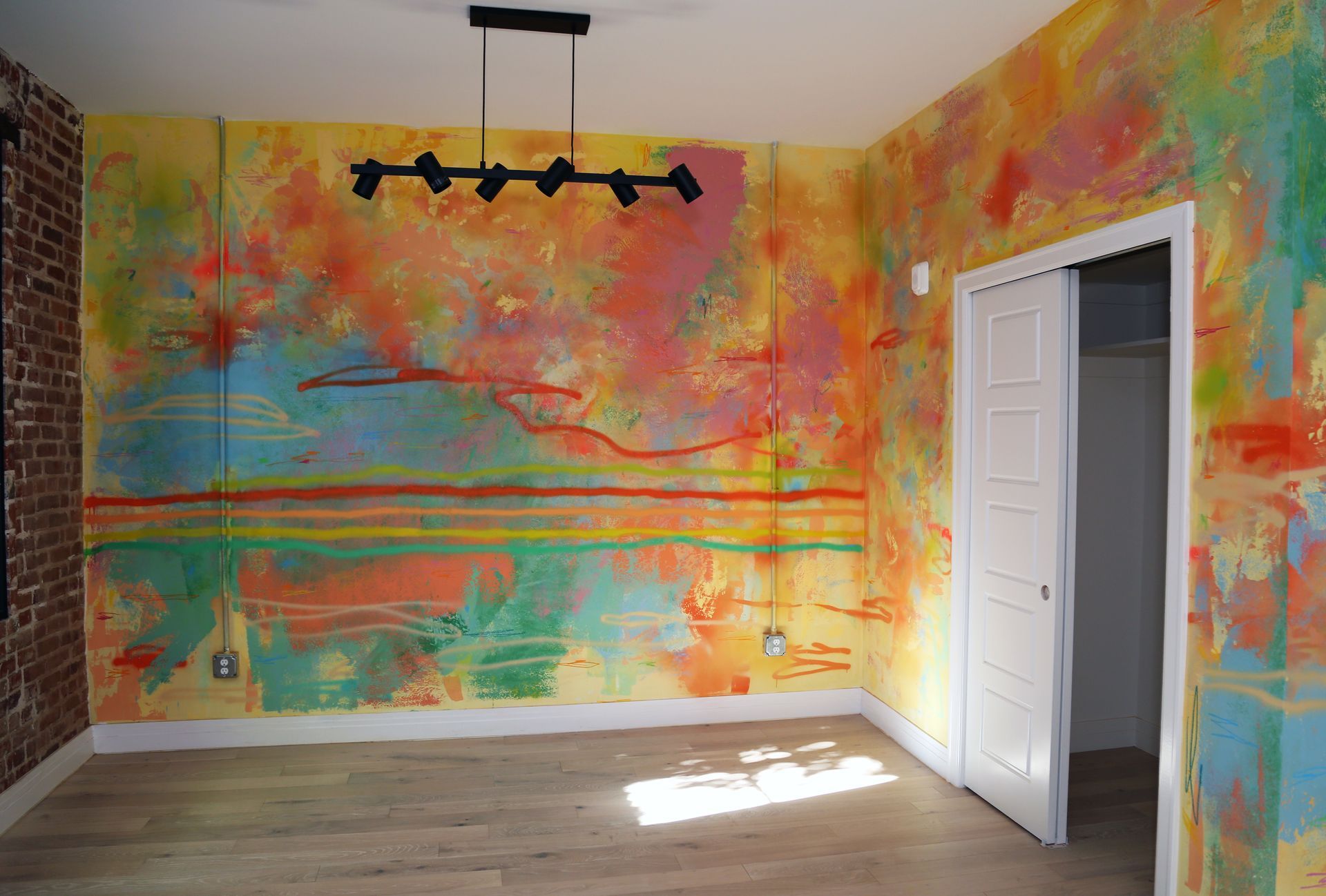Colorful painted room with abstract mural walls, hanging black light fixture, and open white door.