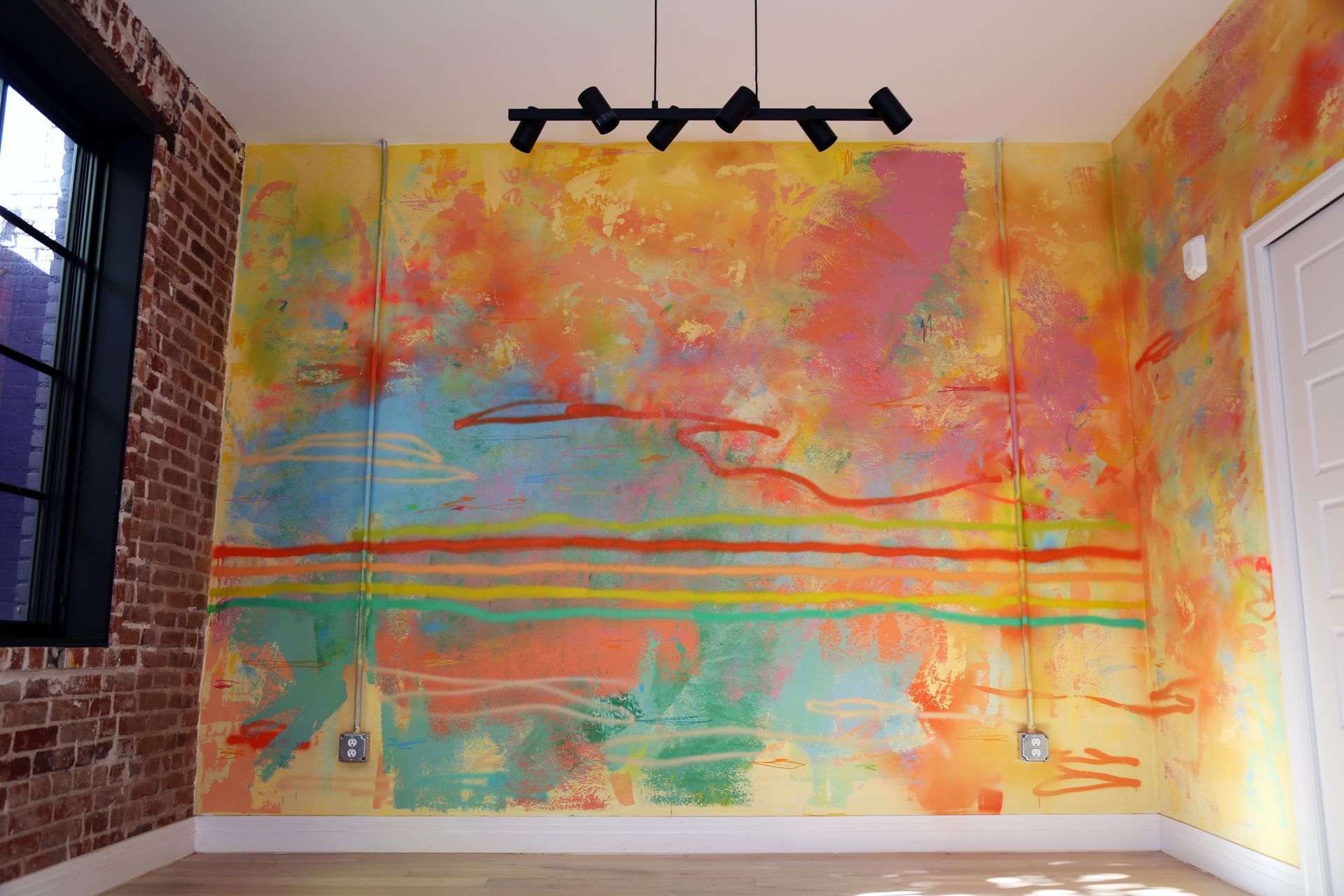 Colorful abstract mural on a room wall with orange, pink, teal, and yellow brushstrokes