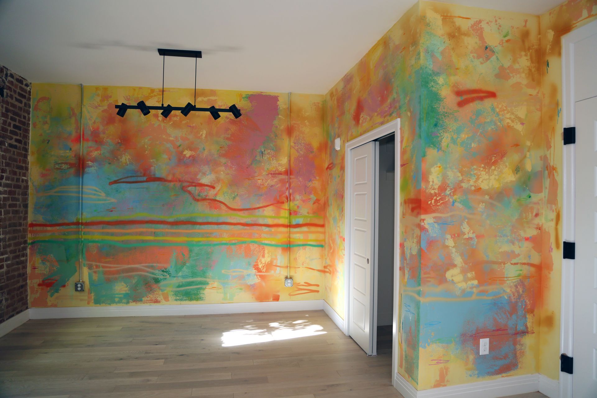 Colorful abstract mural painted on a room’s walls and ceiling with a doorway and floor lamp track.