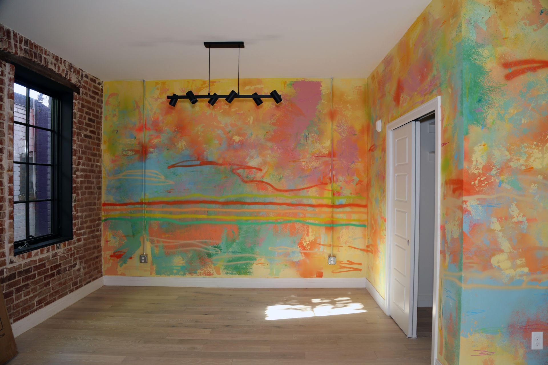 Empty room with colorful abstract mural walls, brick window wall, and hanging light fixture