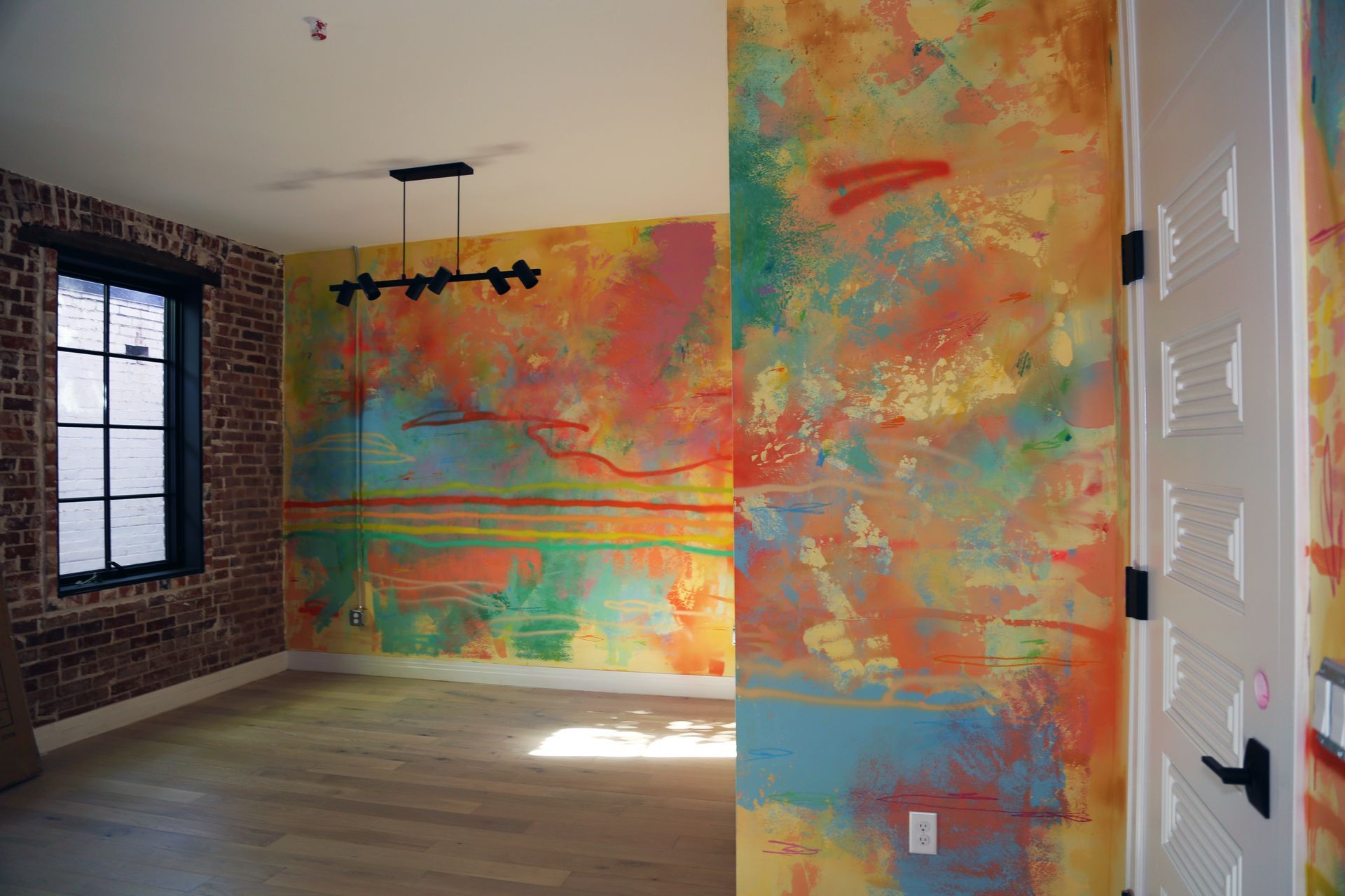 Empty room with colorful abstract painted walls, brick accent wall, and a window letting in light