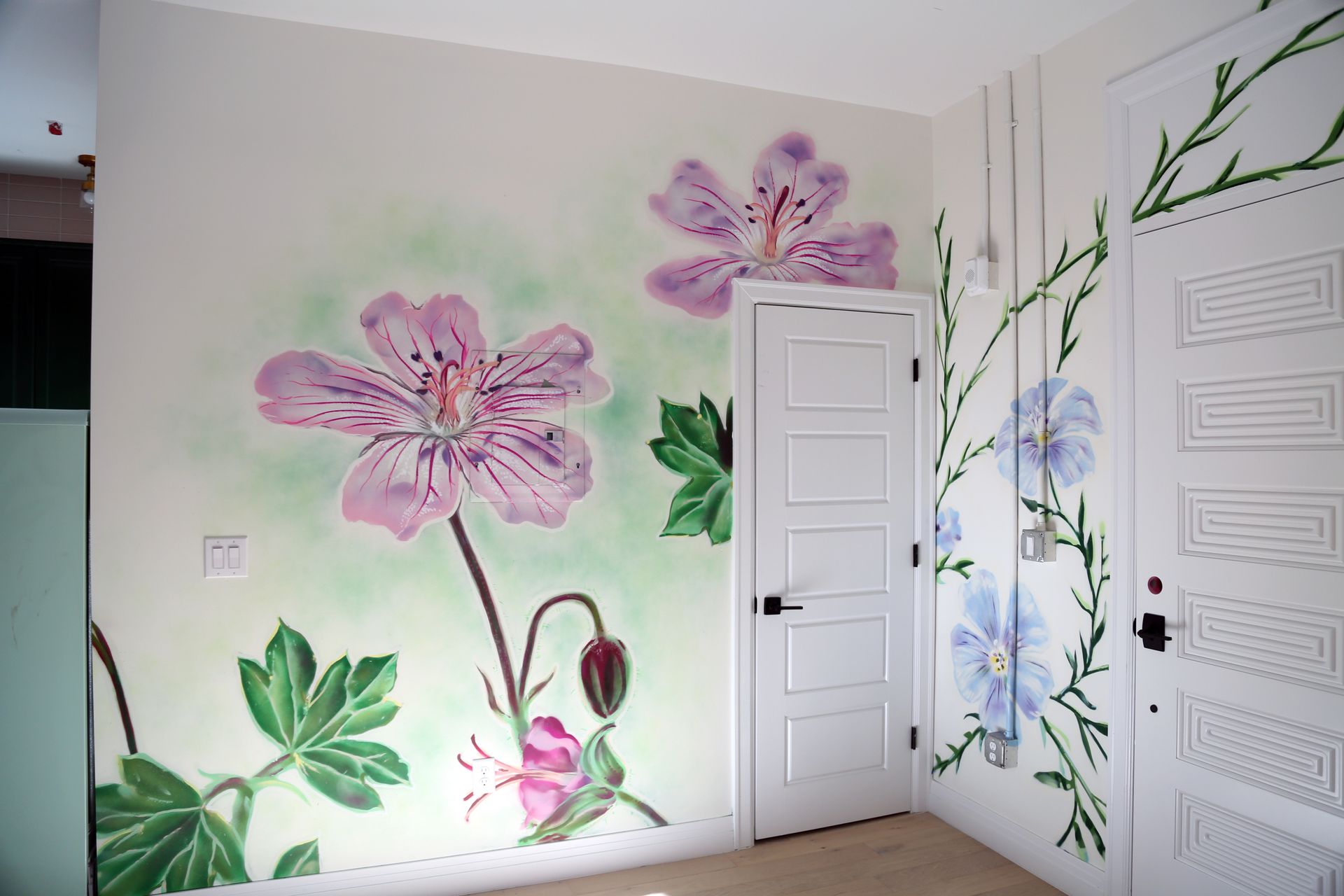 Flower mural on white bedroom walls with large pink and blue blossoms around two white doors