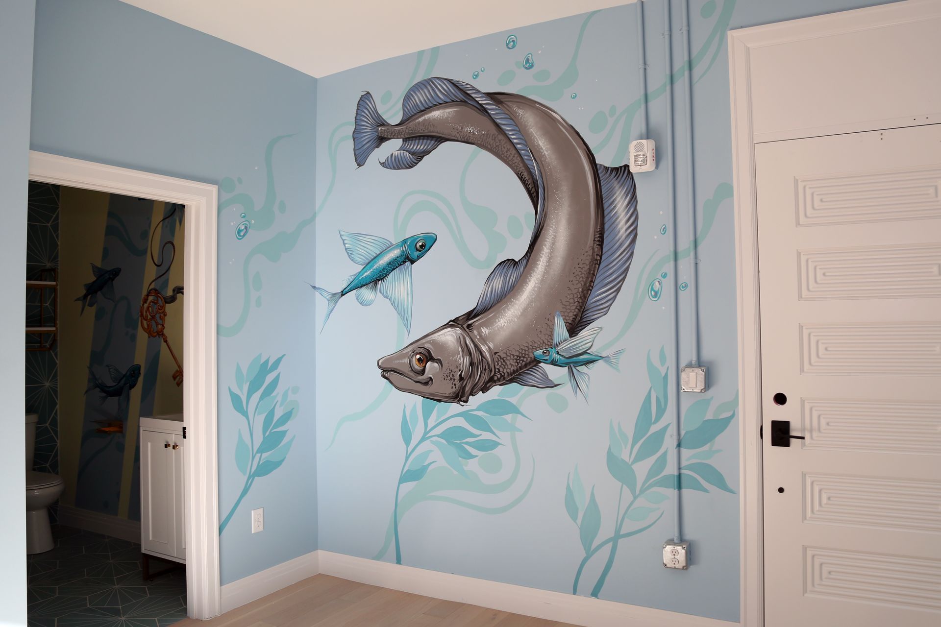 Blue whale wall mural in a child’s room with ocean plants and a fish, beside a white door.