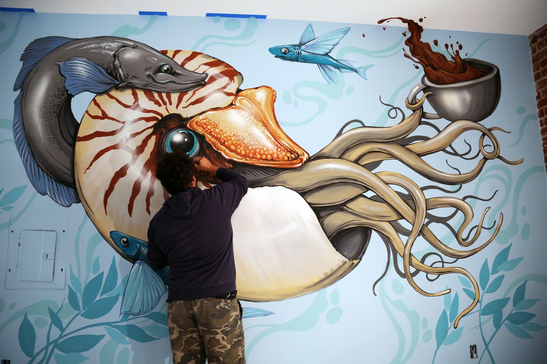 Person painting a large colorful octopus mural on a wall