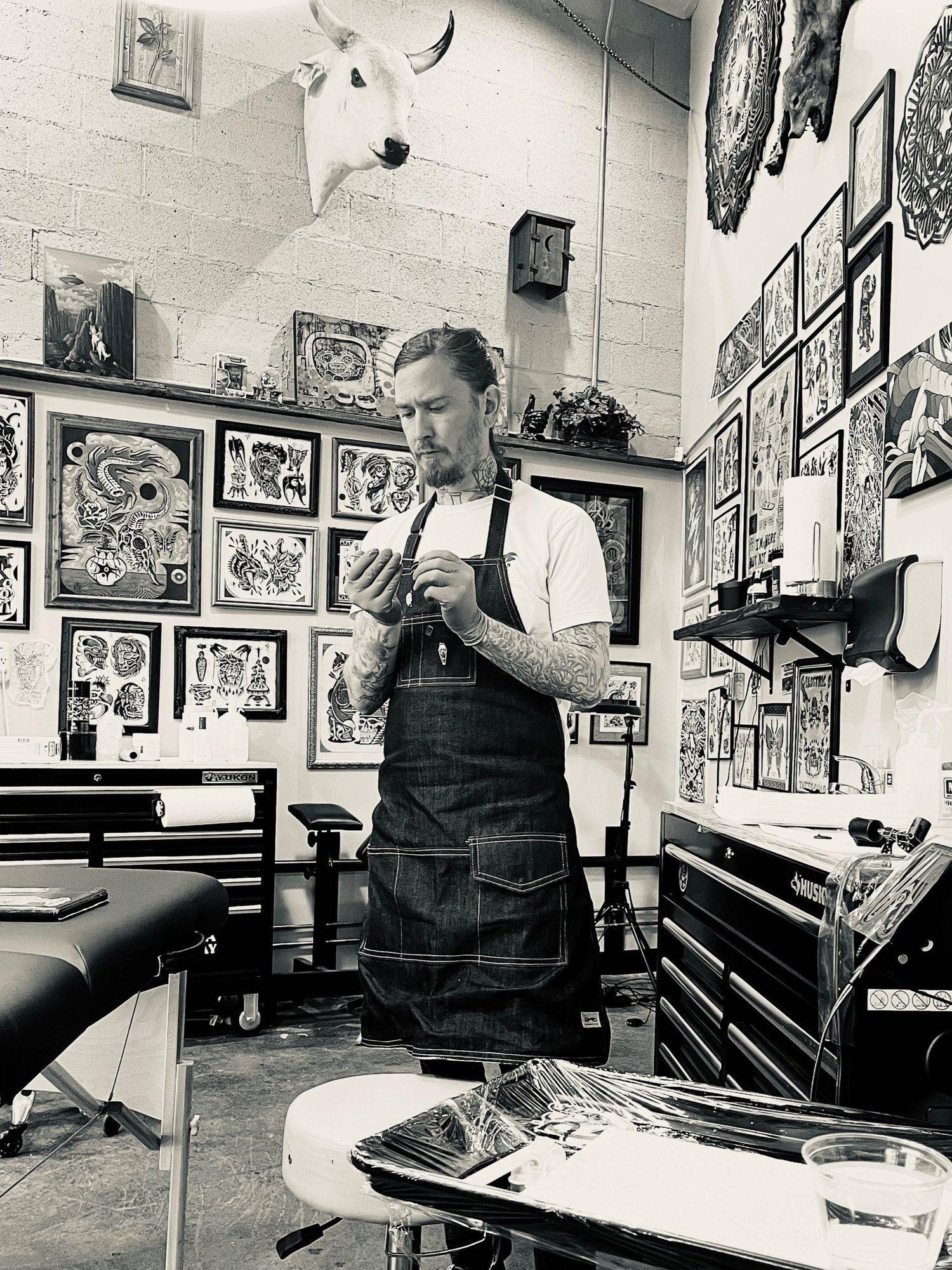 Tattoo artist in an apron working in a tattoo studio surrounded by framed artwork