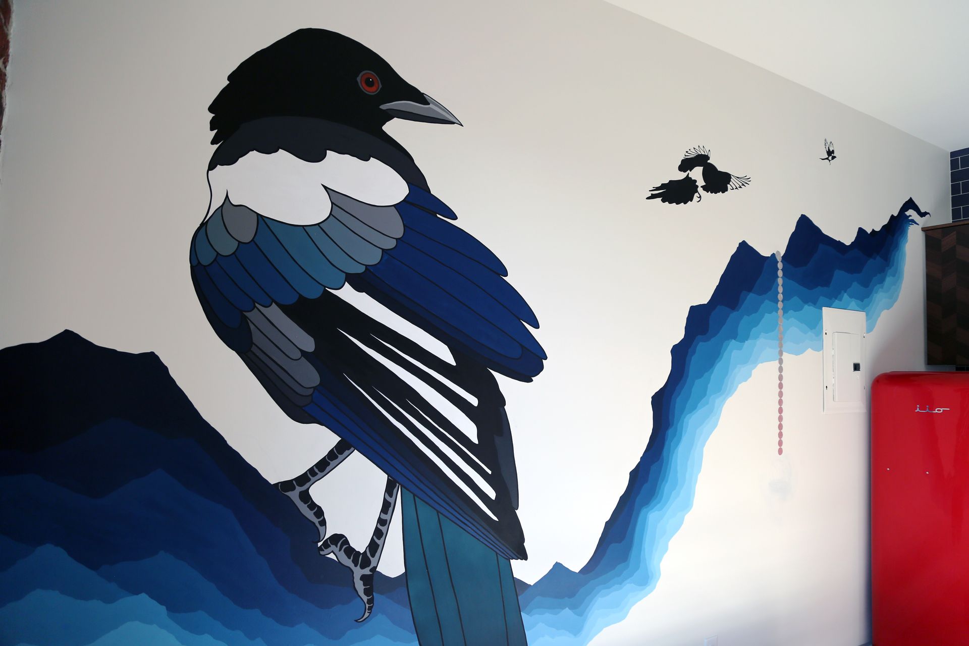 Mural of a black-and-blue bird perched on a branch against a blue mountain-like backdrop
