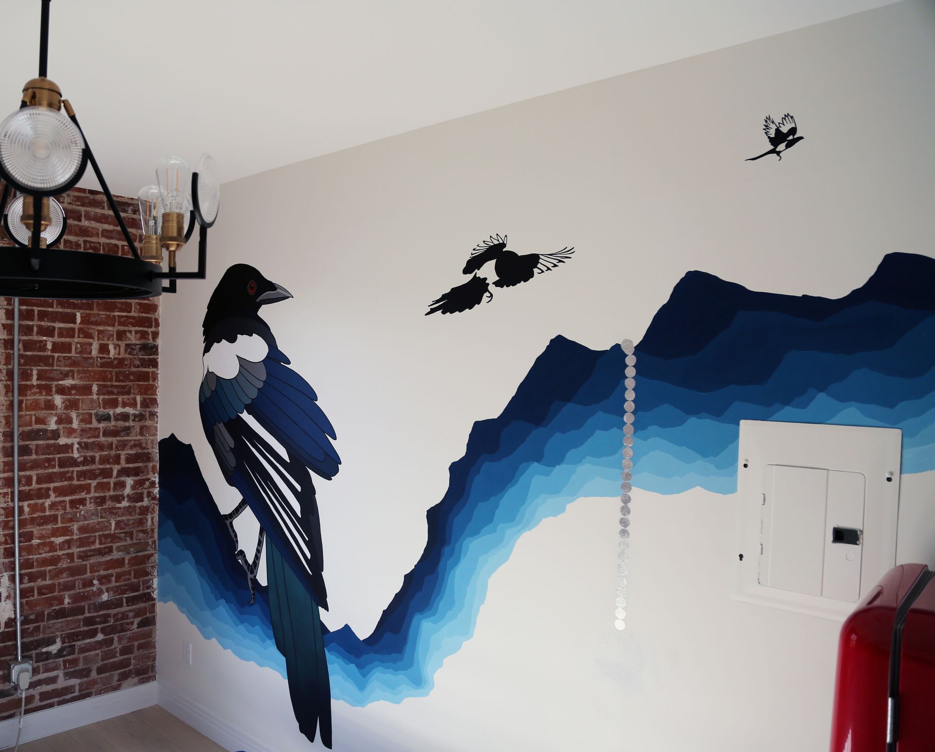 Wall mural with large black-and-blue bird on a brick-and-white wall, plus smaller flying birds.