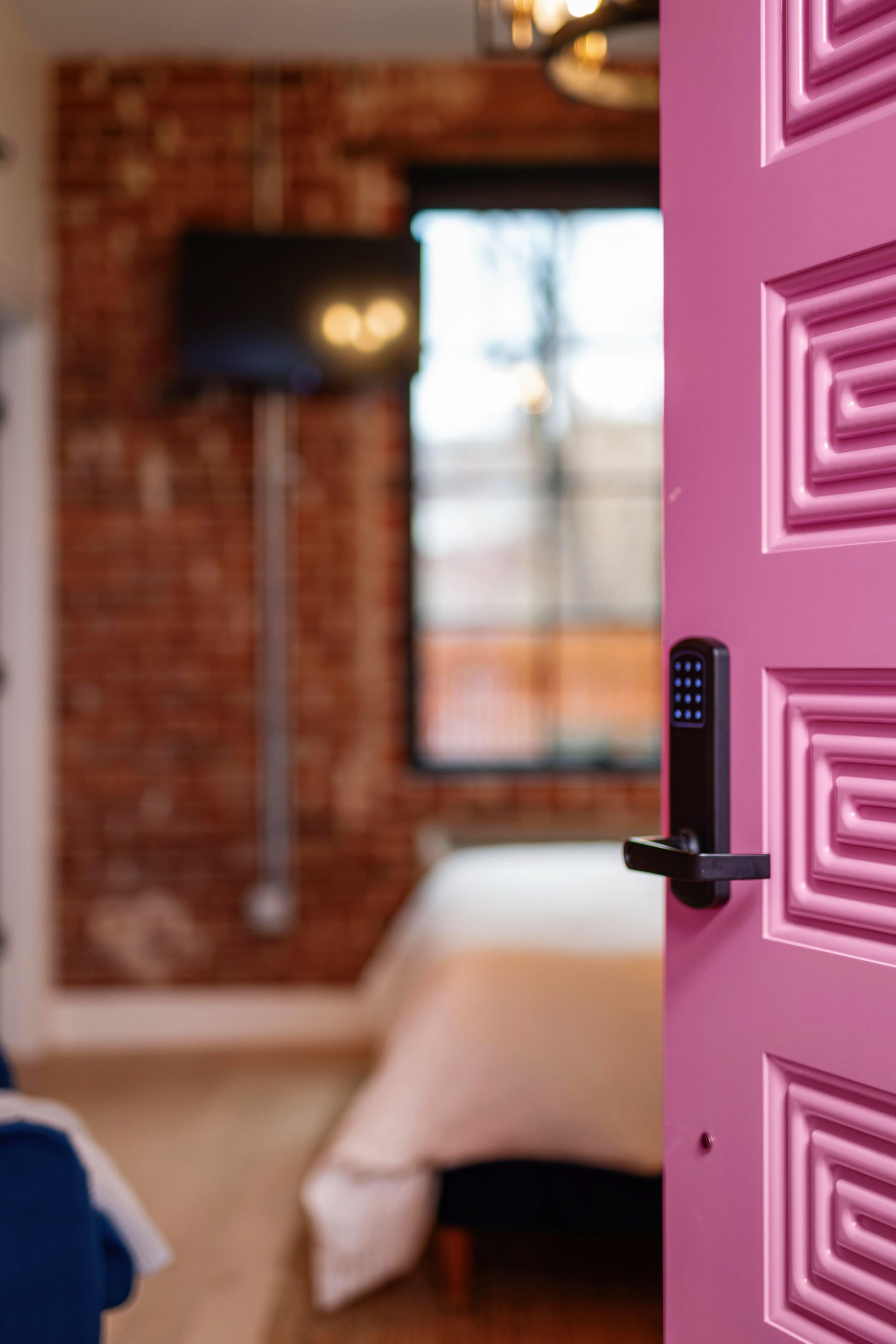 Open pink door with geometric design into a cozy brick-walled bedroom
