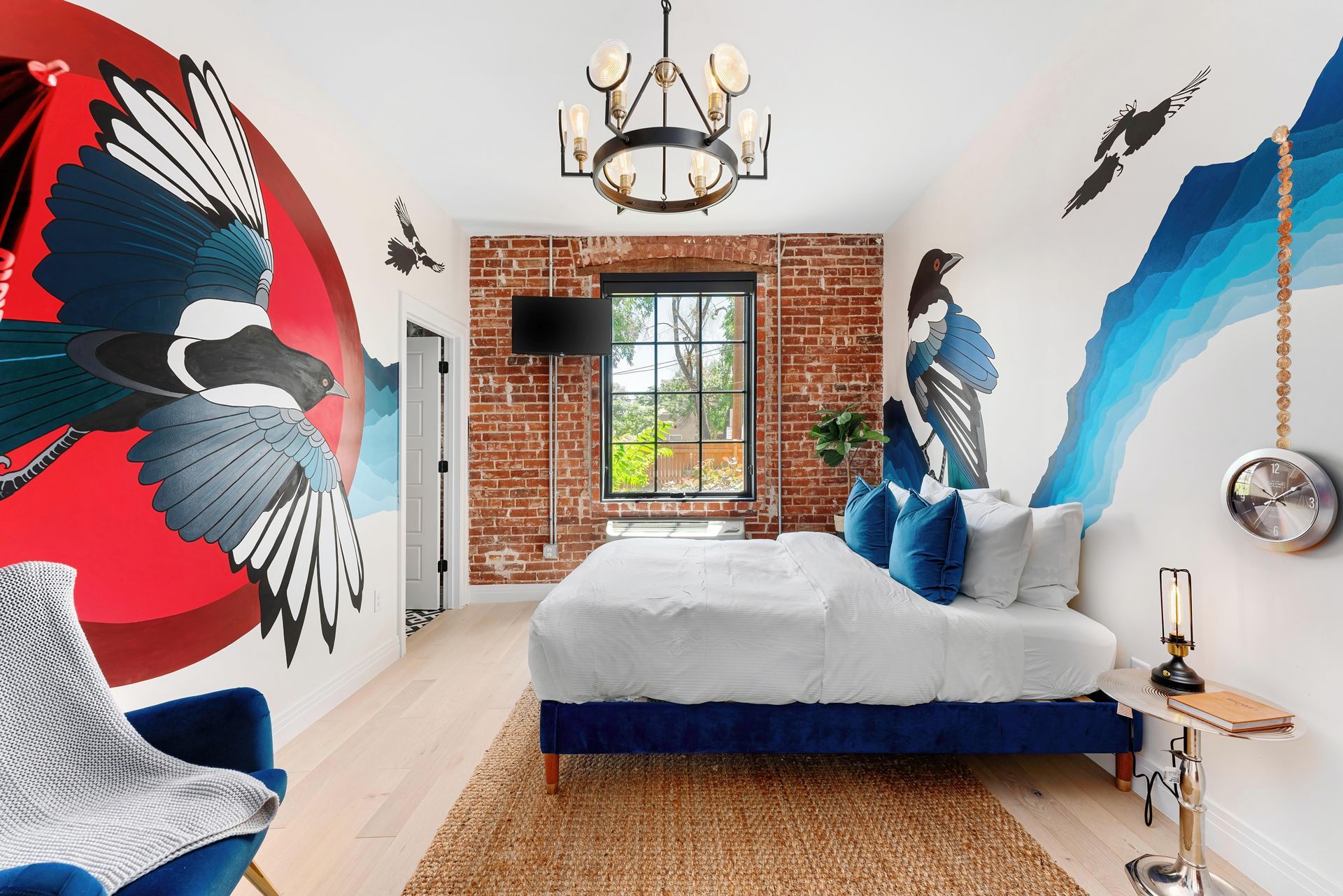 Colorful bedroom with bird murals, blue bed, brick accent wall, and window-centered décor