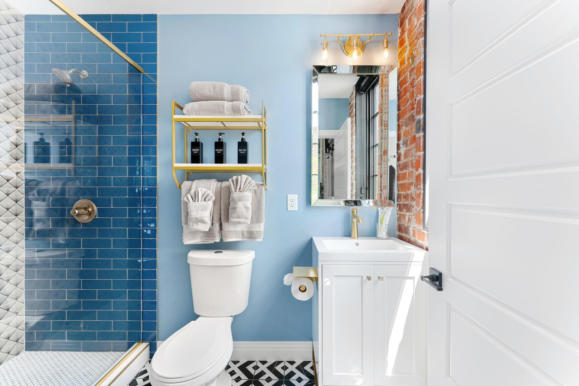 Bright bathroom with blue tile shower, white vanity, mirror, and black-and-white patterned floor.