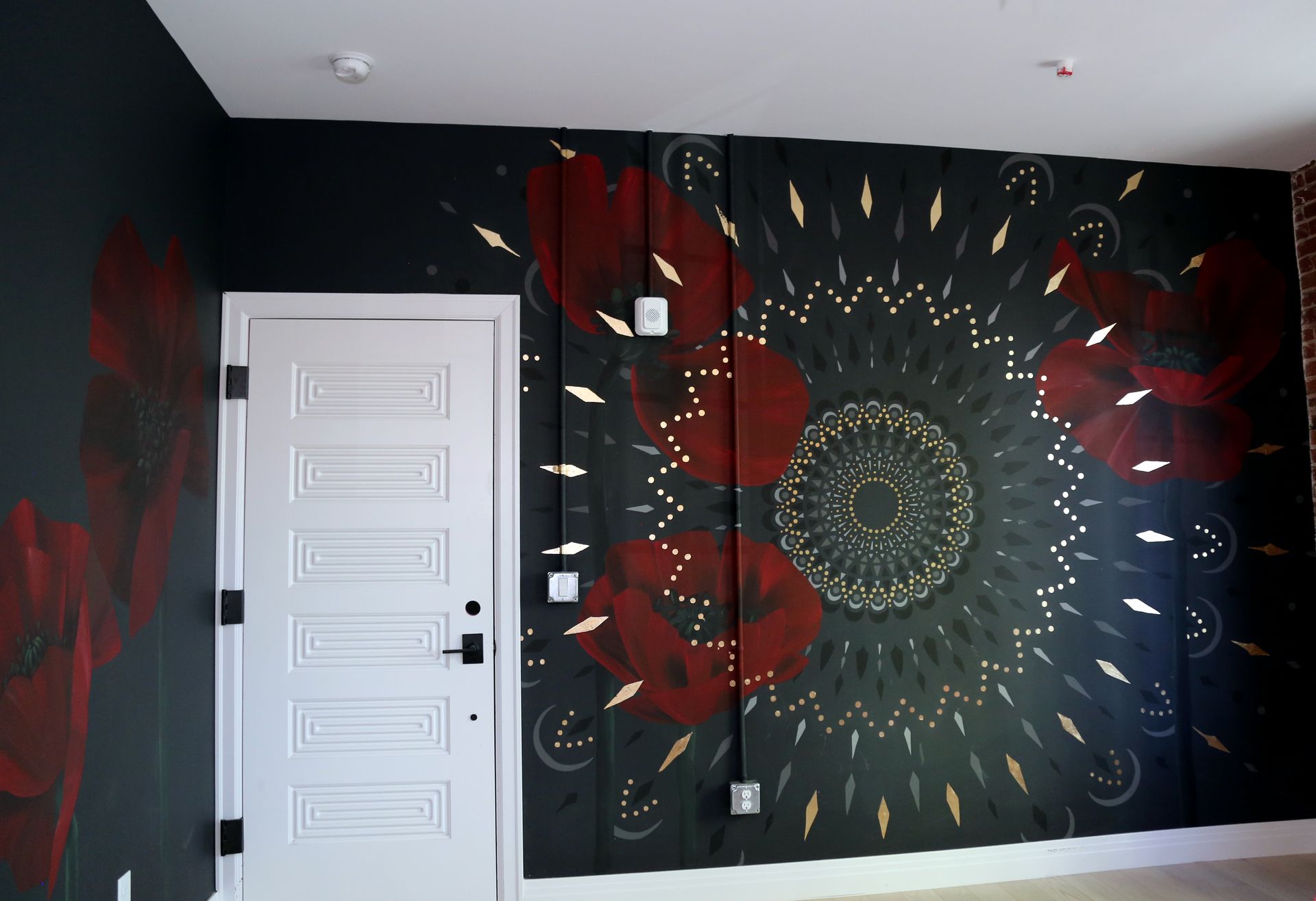 Black room wall with large red and gold mandala mural beside a white door
