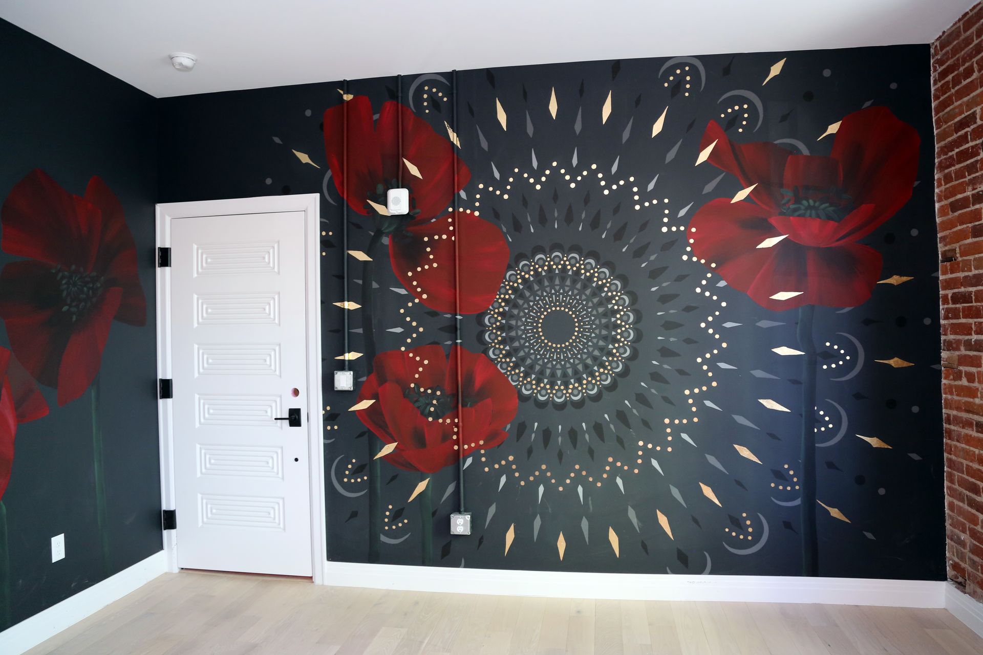 Black room with large red floral mural and circular mandala pattern beside a white door