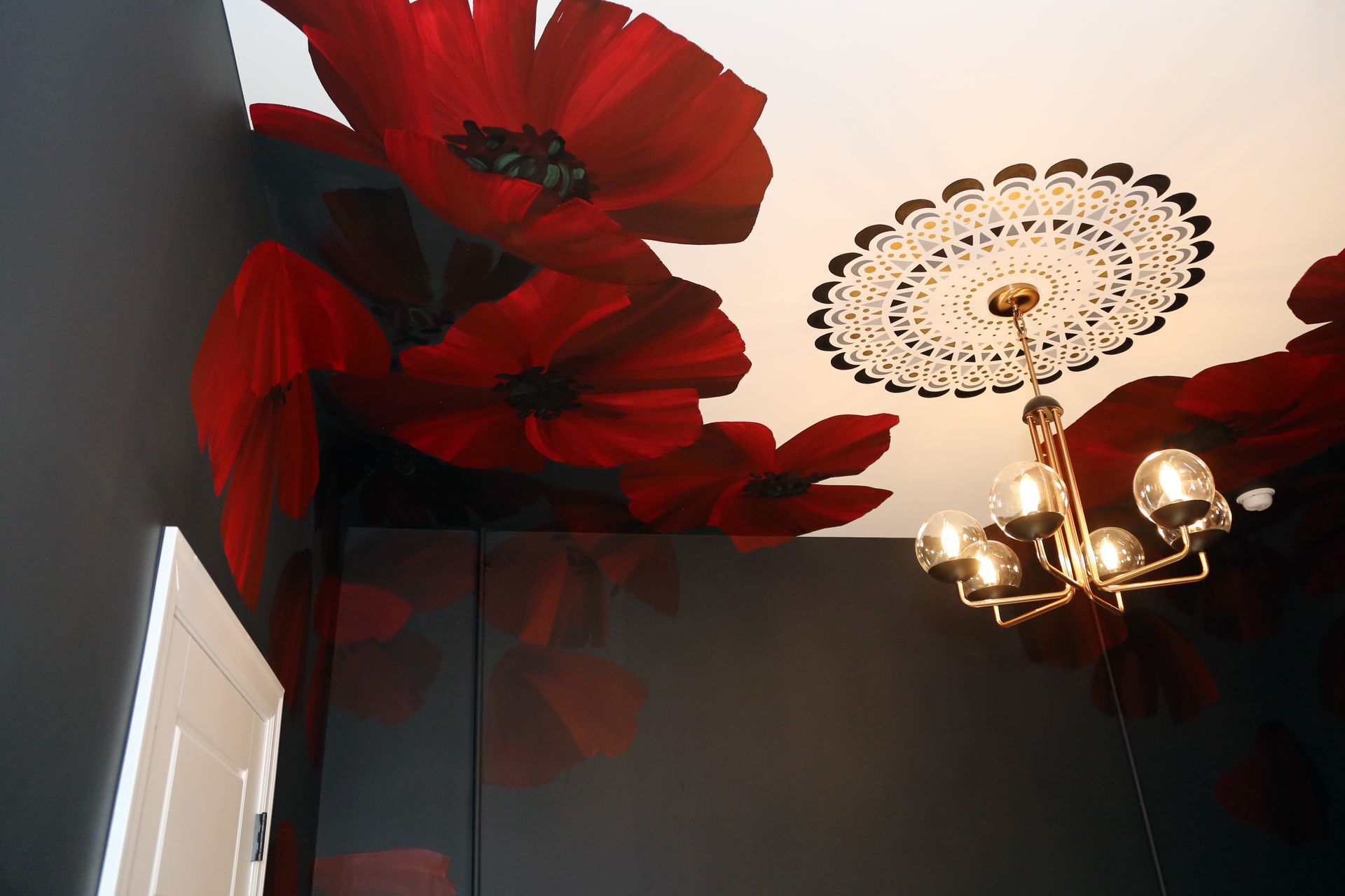 Red paper flowers on a dark ceiling beside a white chandelier and decorative medallion