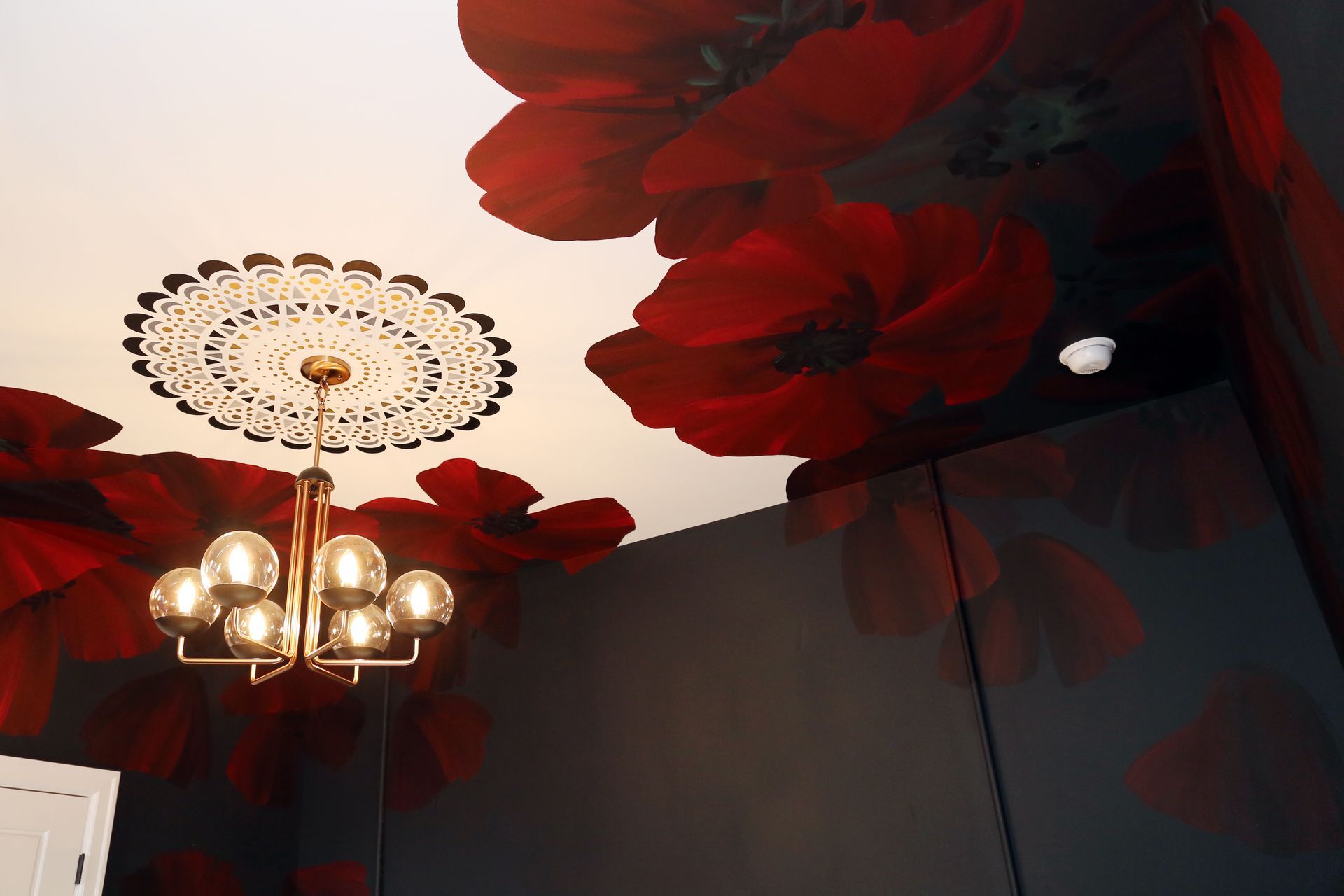Chandelier beneath ornate white ceiling medallion and large red flower mural on dark walls