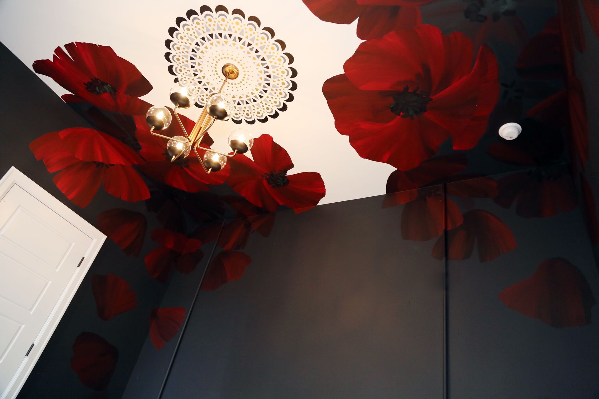 Red flowers on a dark wall and ceiling around a white chandelier in a room