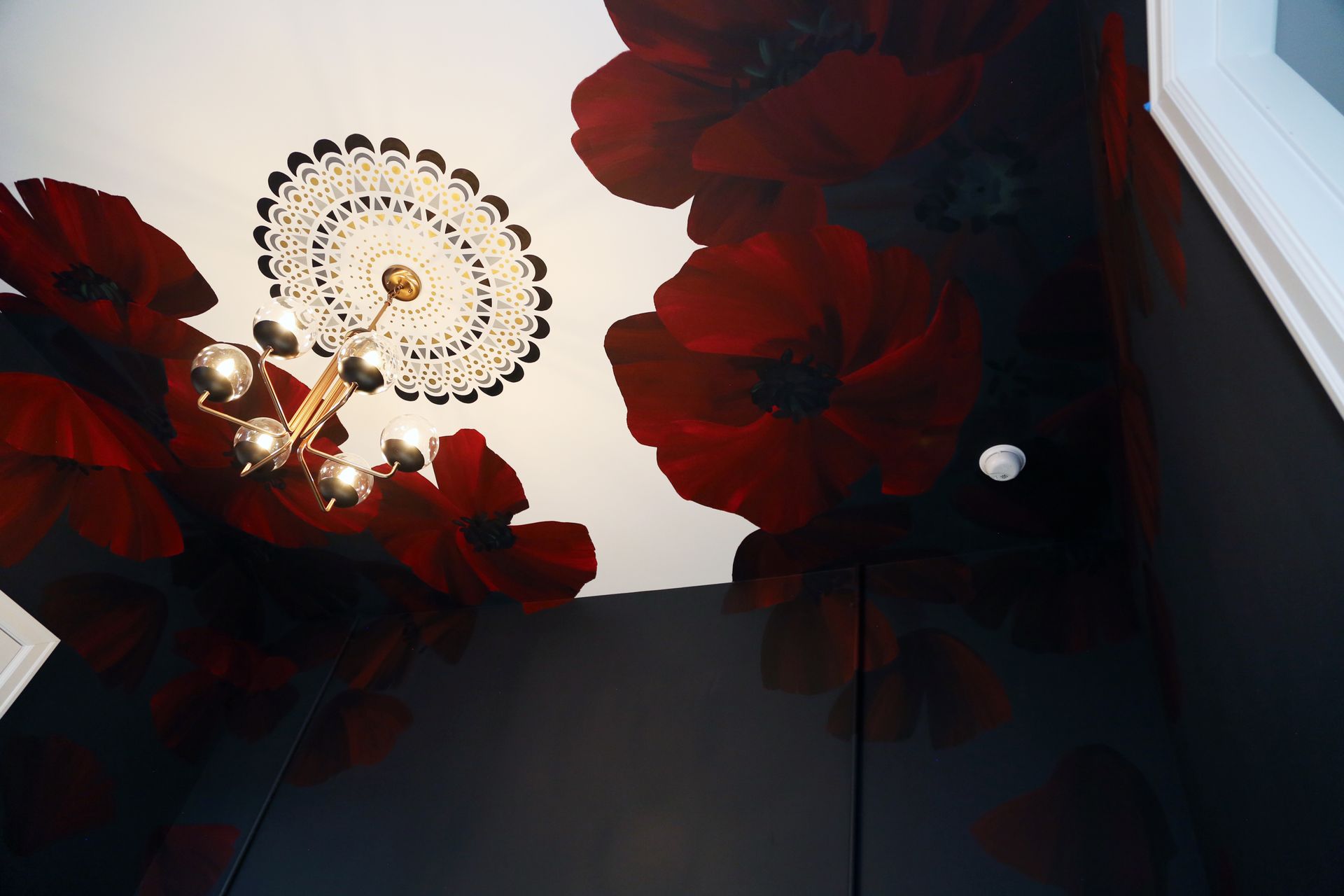 Upward view of a chandelier with red flower-shaped lights on a white ceiling and dark walls
