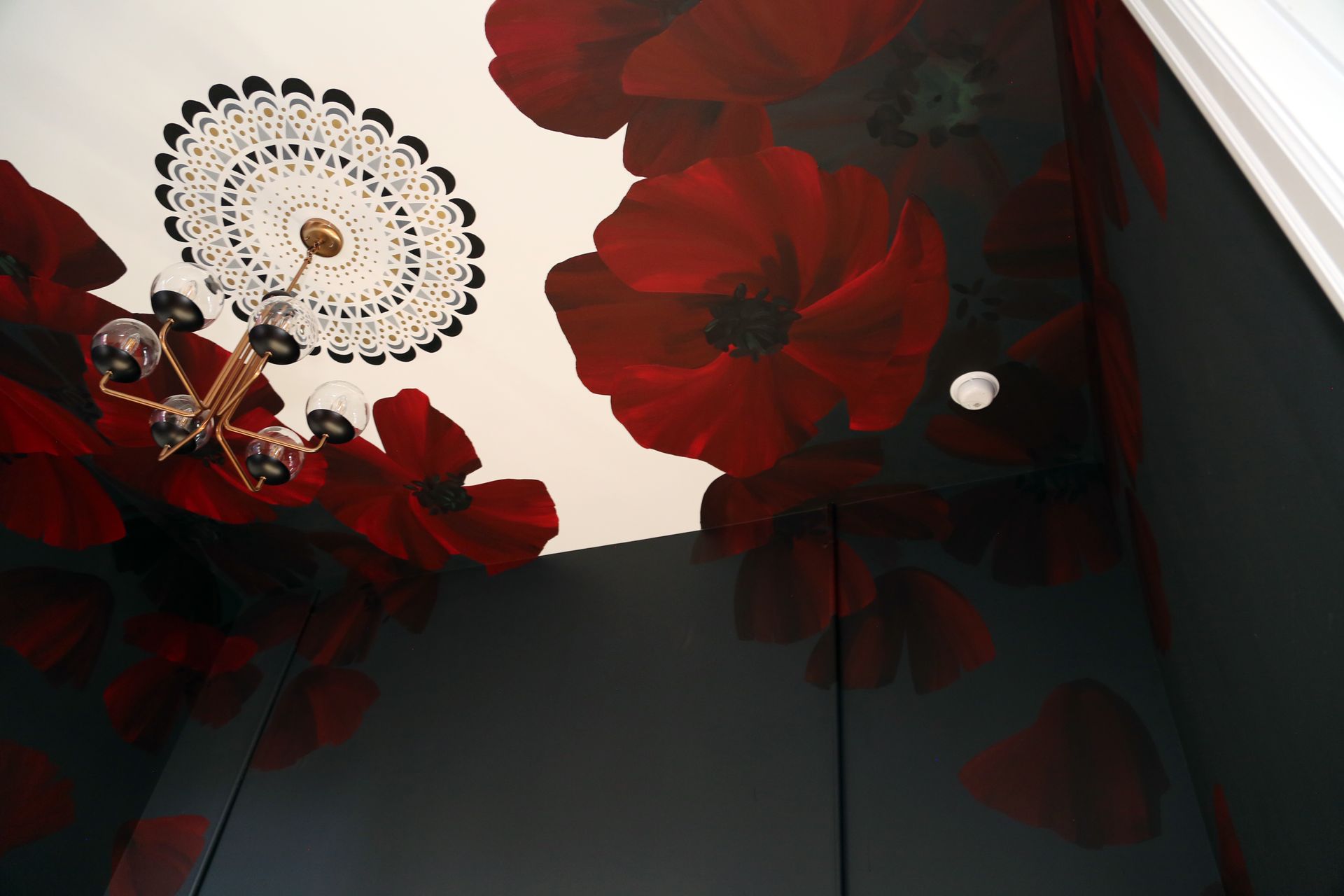 Red flowers and a decorative ceiling light seen from below against a white ceiling