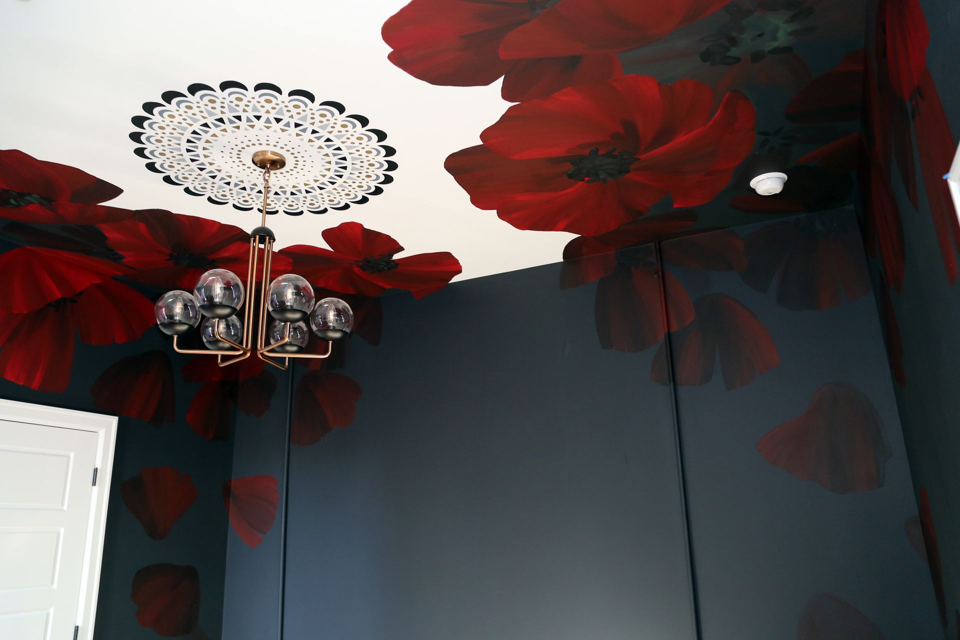 Dark blue room with large red floral ceiling mural and a decorative chandelier