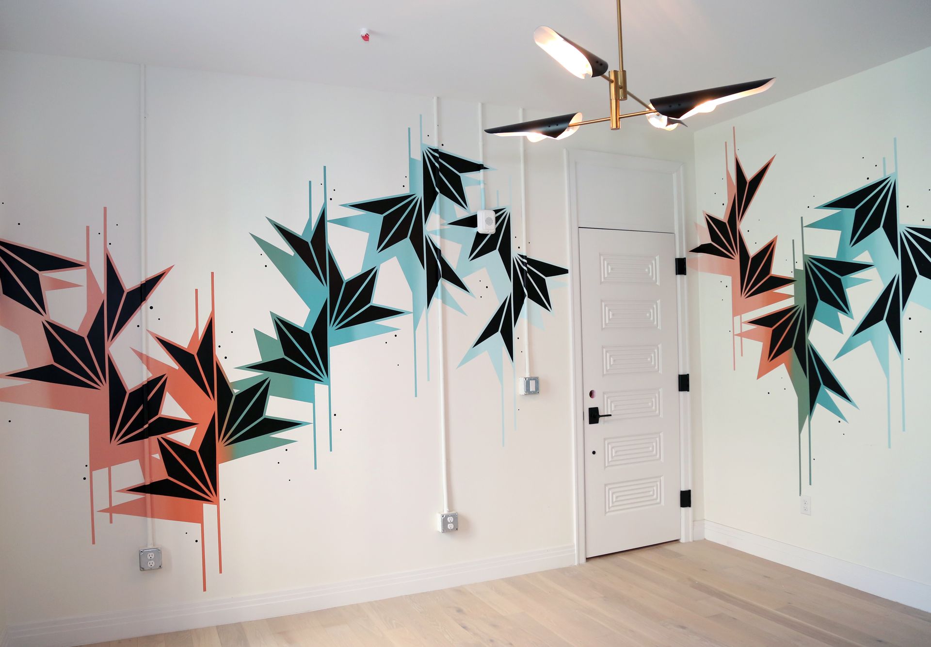 White room with black, teal, and coral geometric wall mural around a door and ceiling fan.