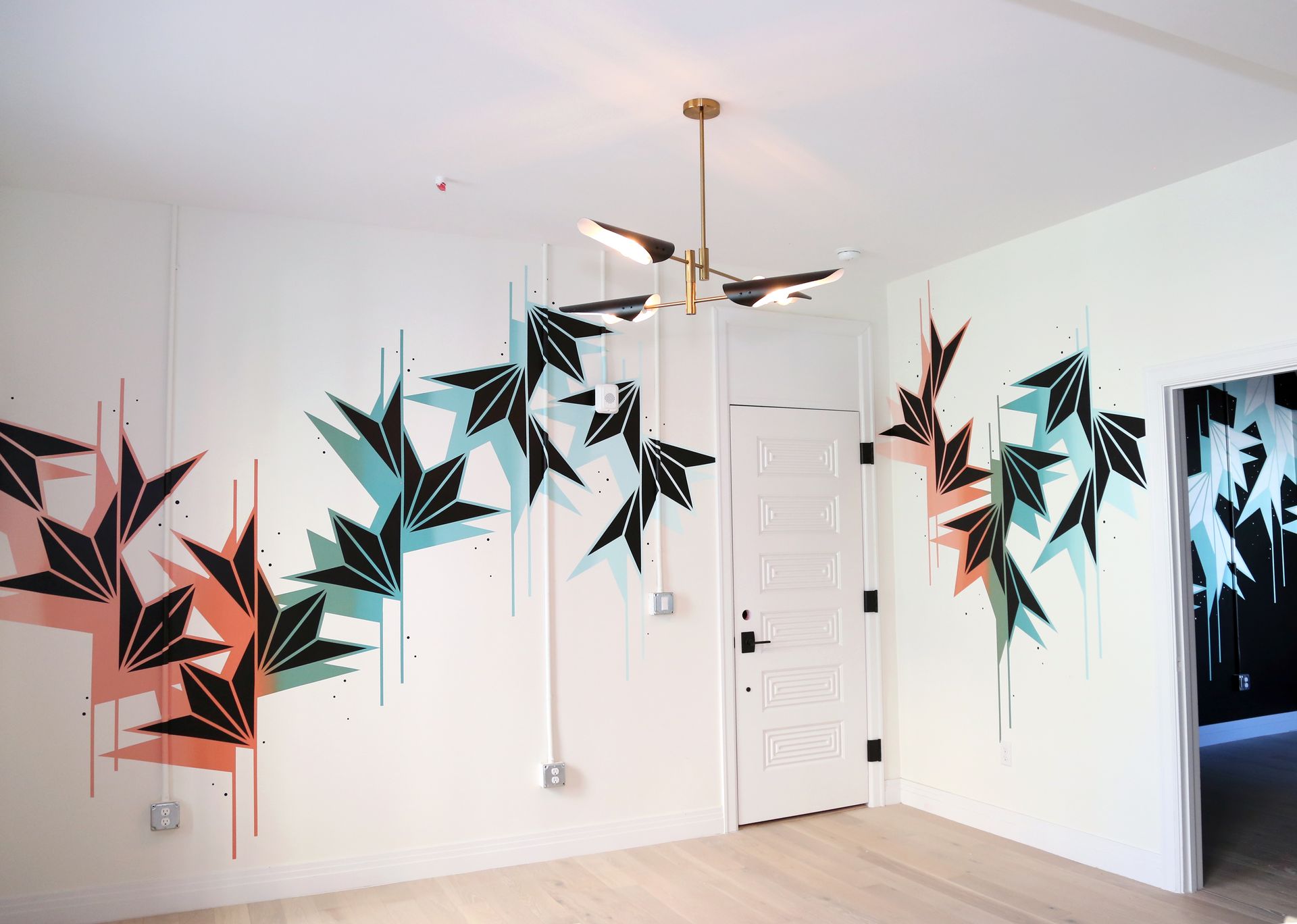 White room with bold black, teal, and coral geometric wall mural and a hanging light fixture
