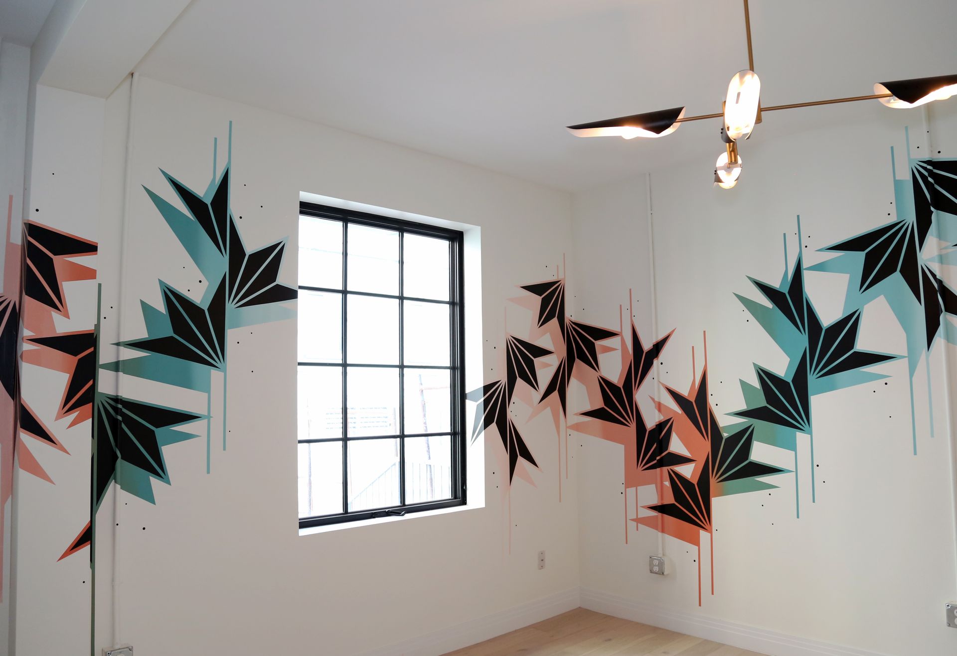 Empty room with black, teal, and pink geometric wall murals around a window
