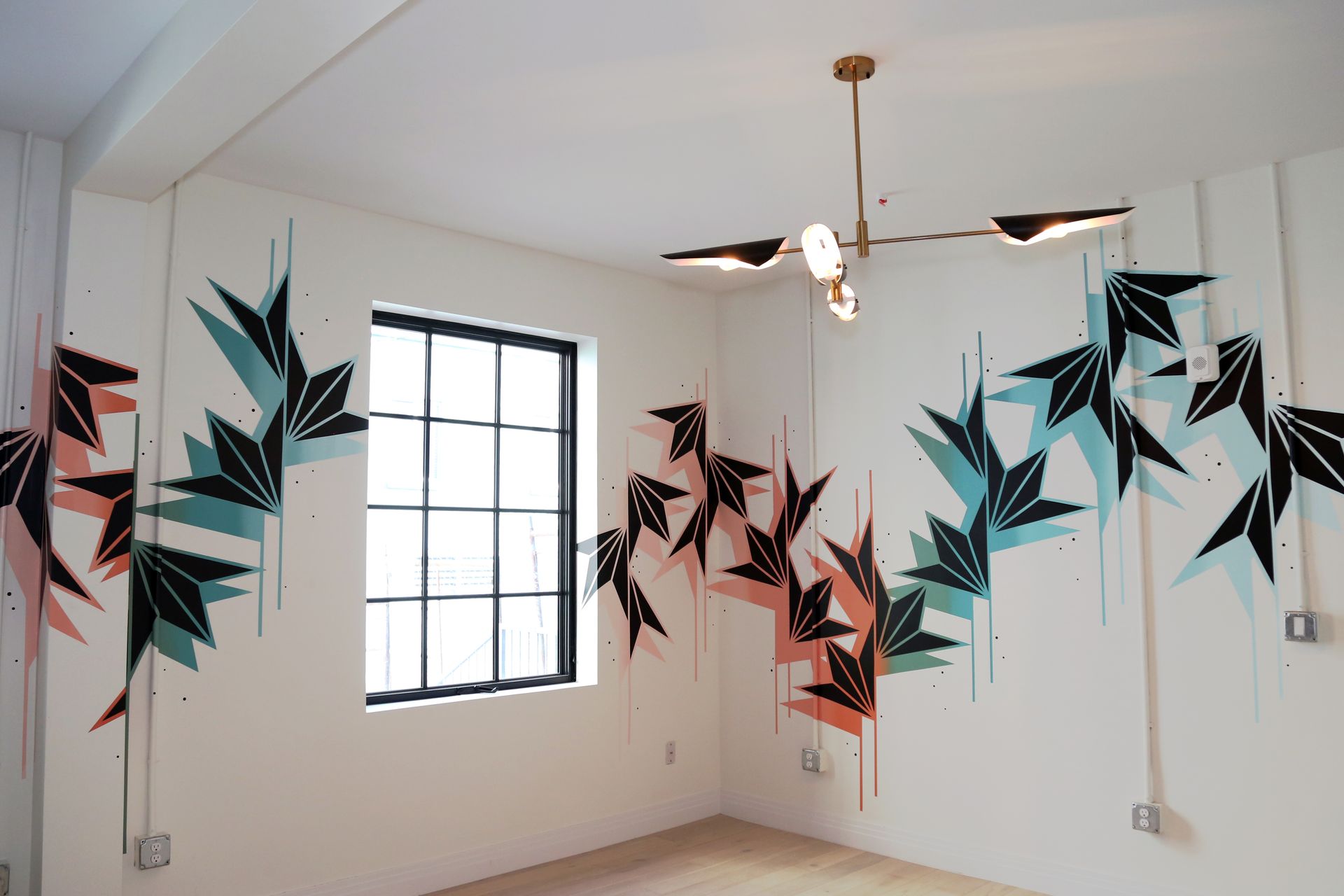 Empty room with geometric teal, black, and pink wall mural, a window, and a ceiling fan light