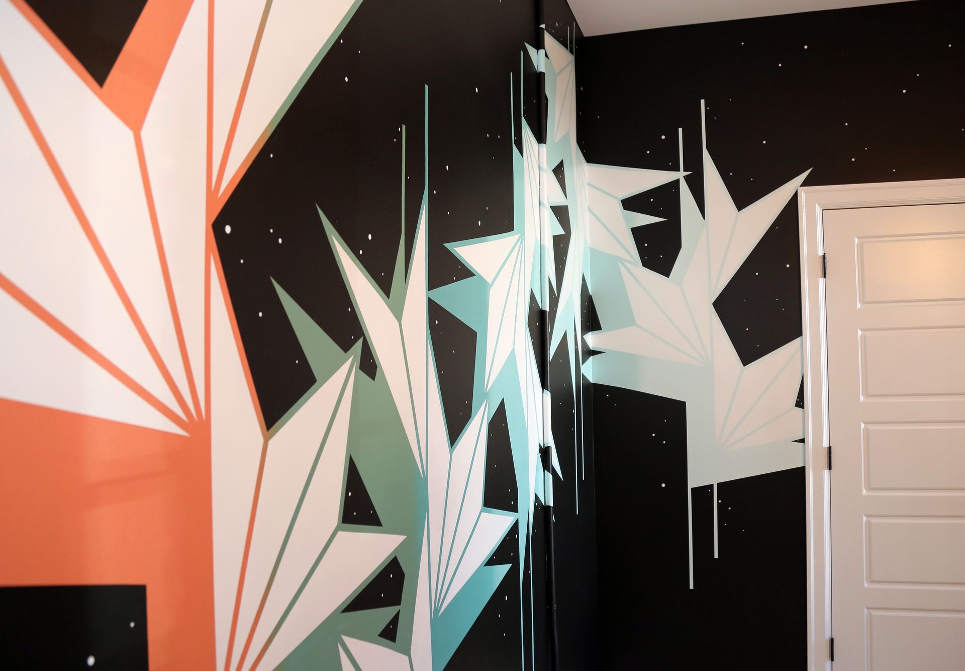 Abstract geometric mural in black, white, mint, and coral on an interior wall beside a door