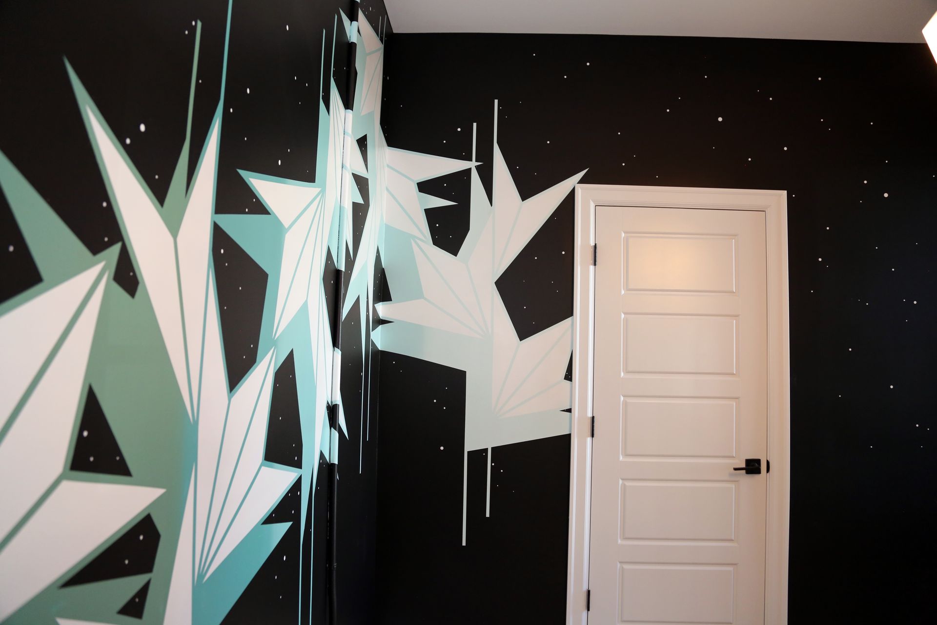 Black wall mural with white geometric shards beside a closed white door and starry ceiling.