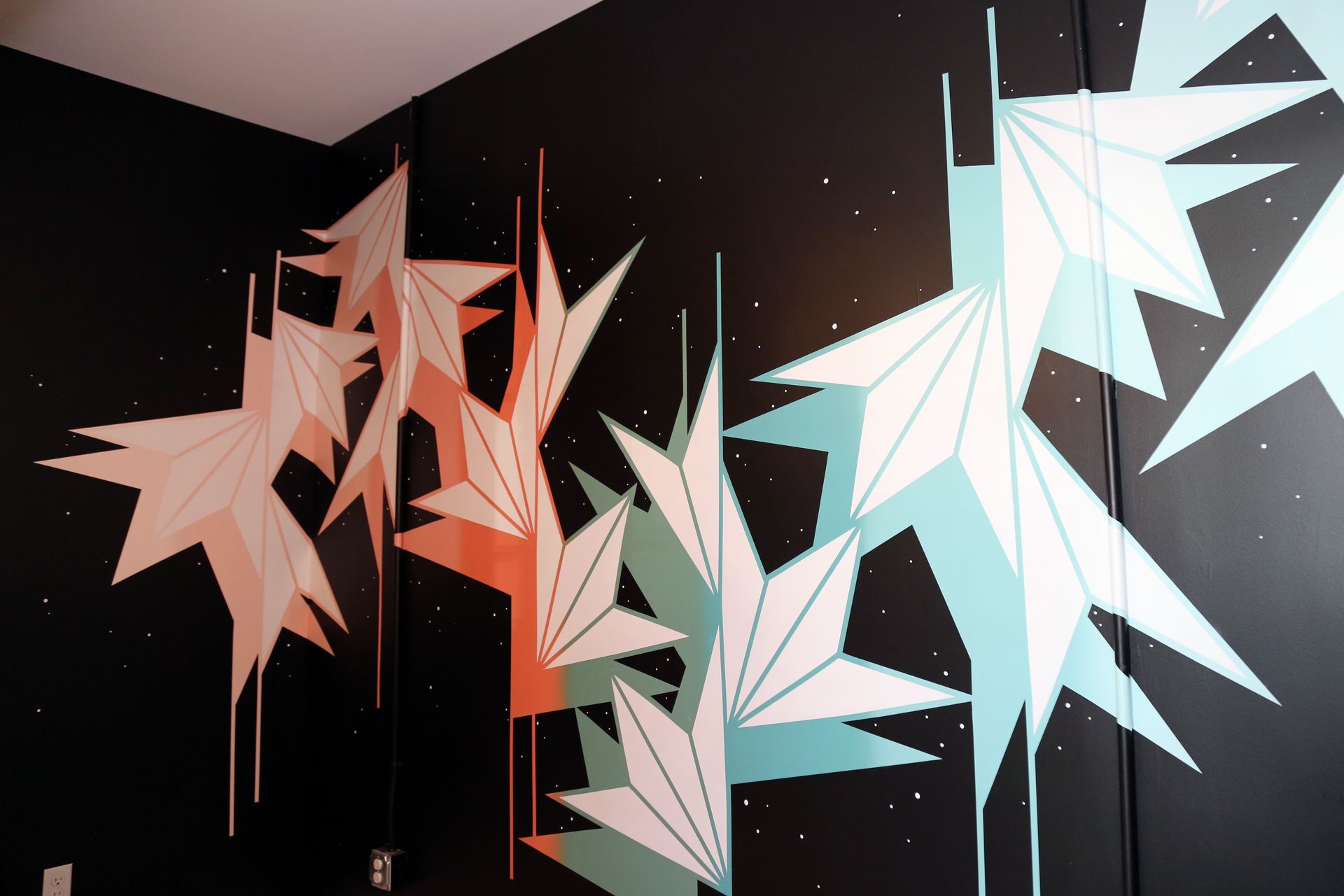 Abstract geometric wall art with pink, black, and white angular shapes on a dark wall
