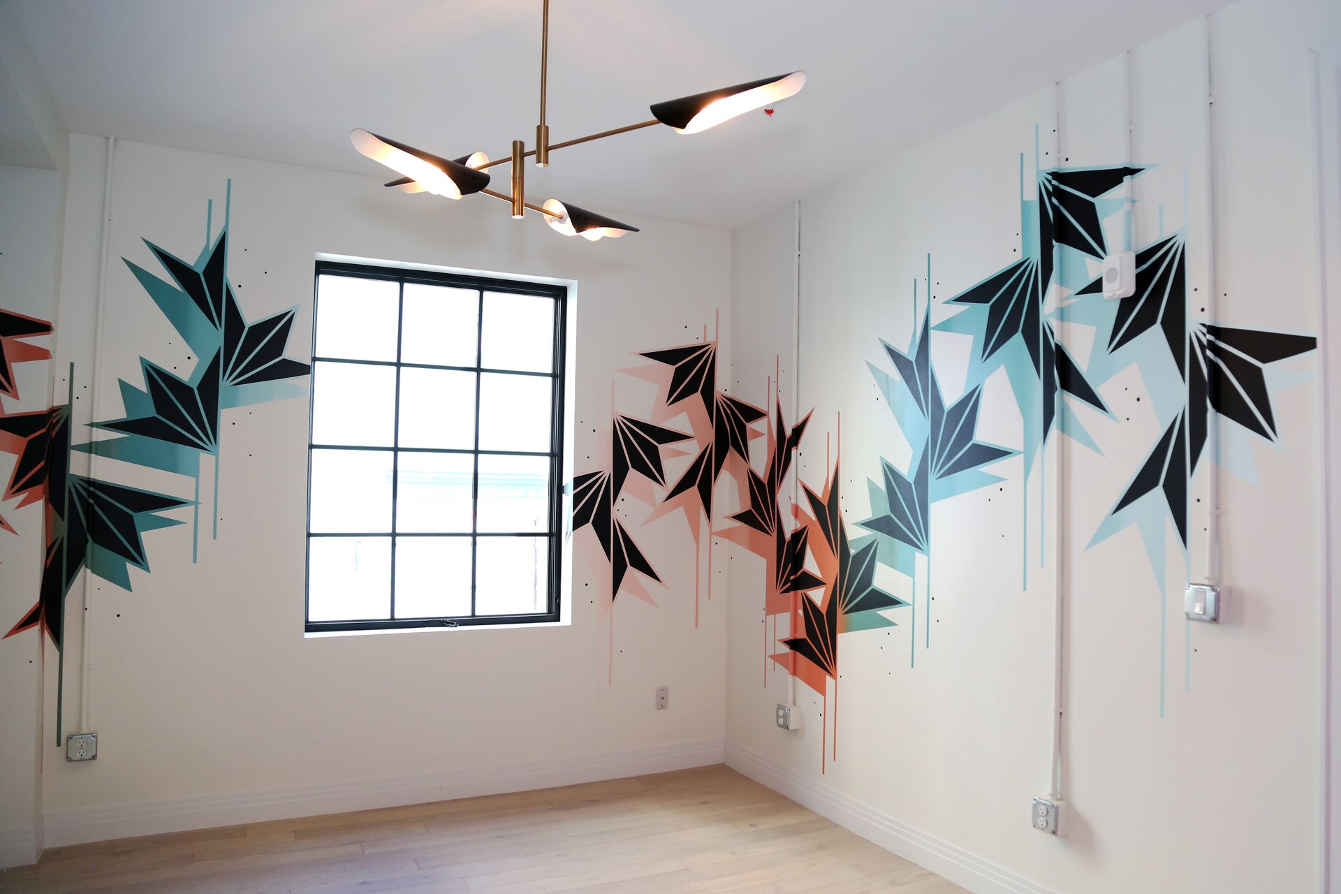 Modern room with geometric wall art in black, teal, and coral around a window and ceiling light fixture