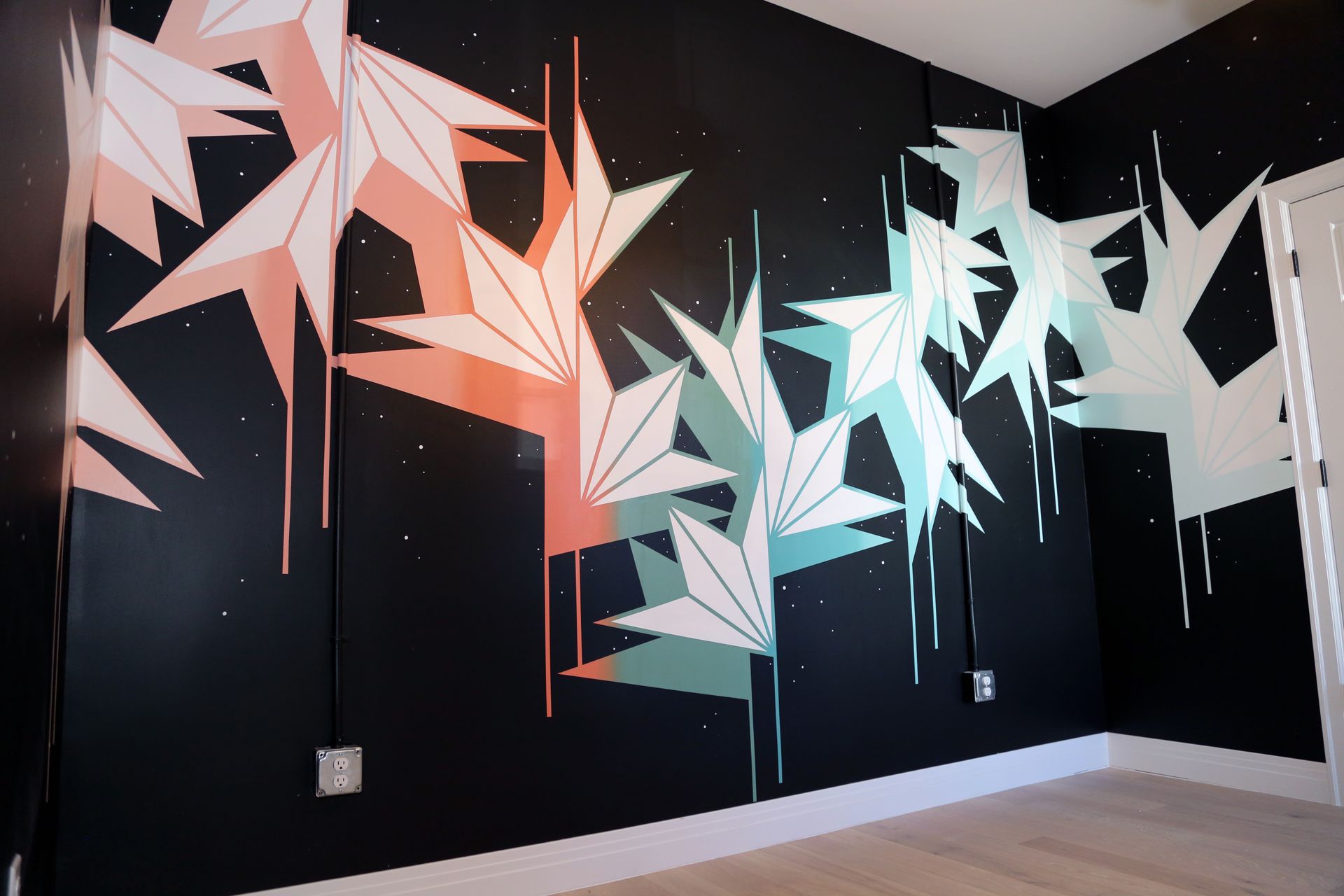 Abstract mural of white, pink, and teal geometric birds on black walls in a corner room