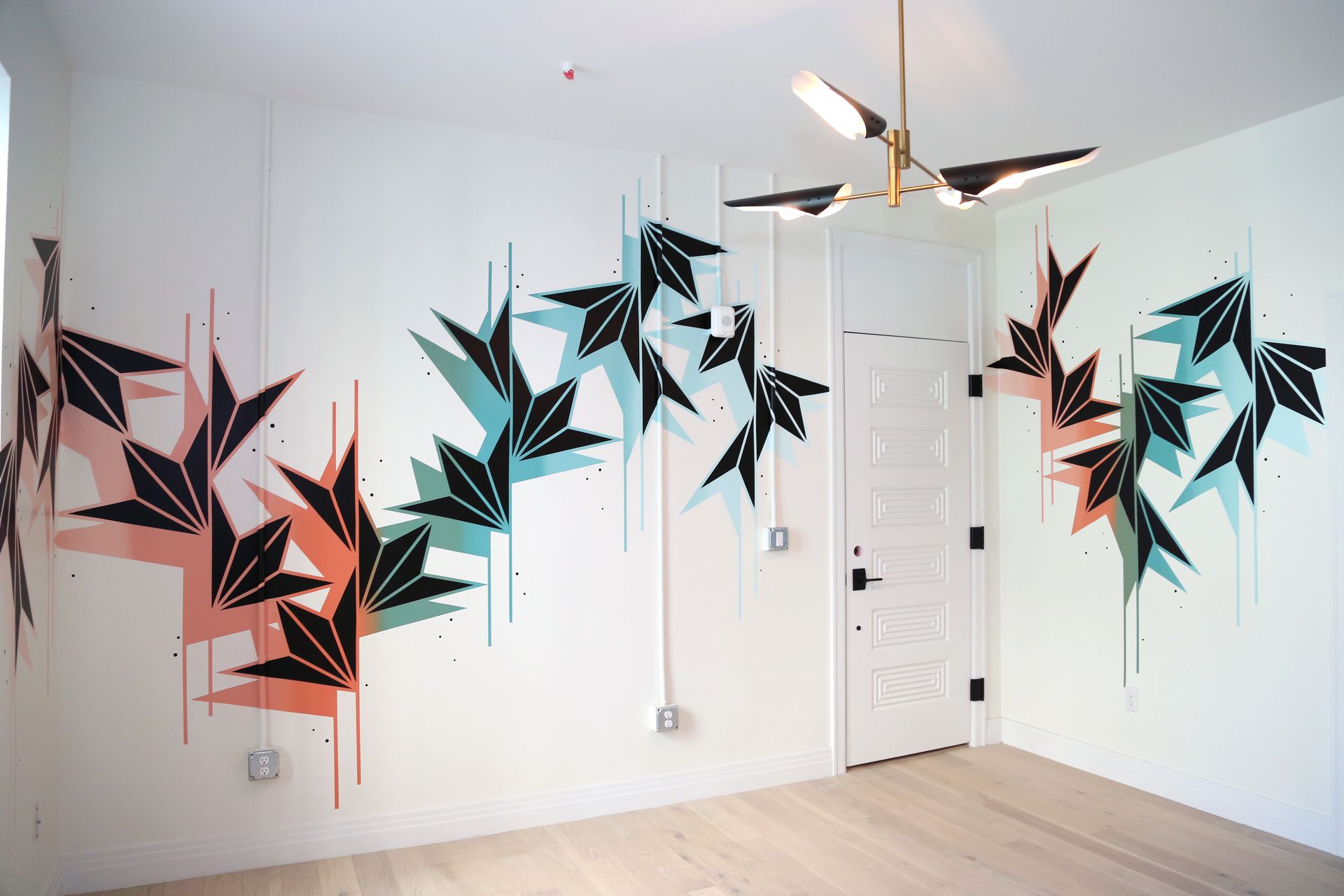 Abstract black, teal, and coral geometric mural painted on a white room wall with a ceiling fan and door