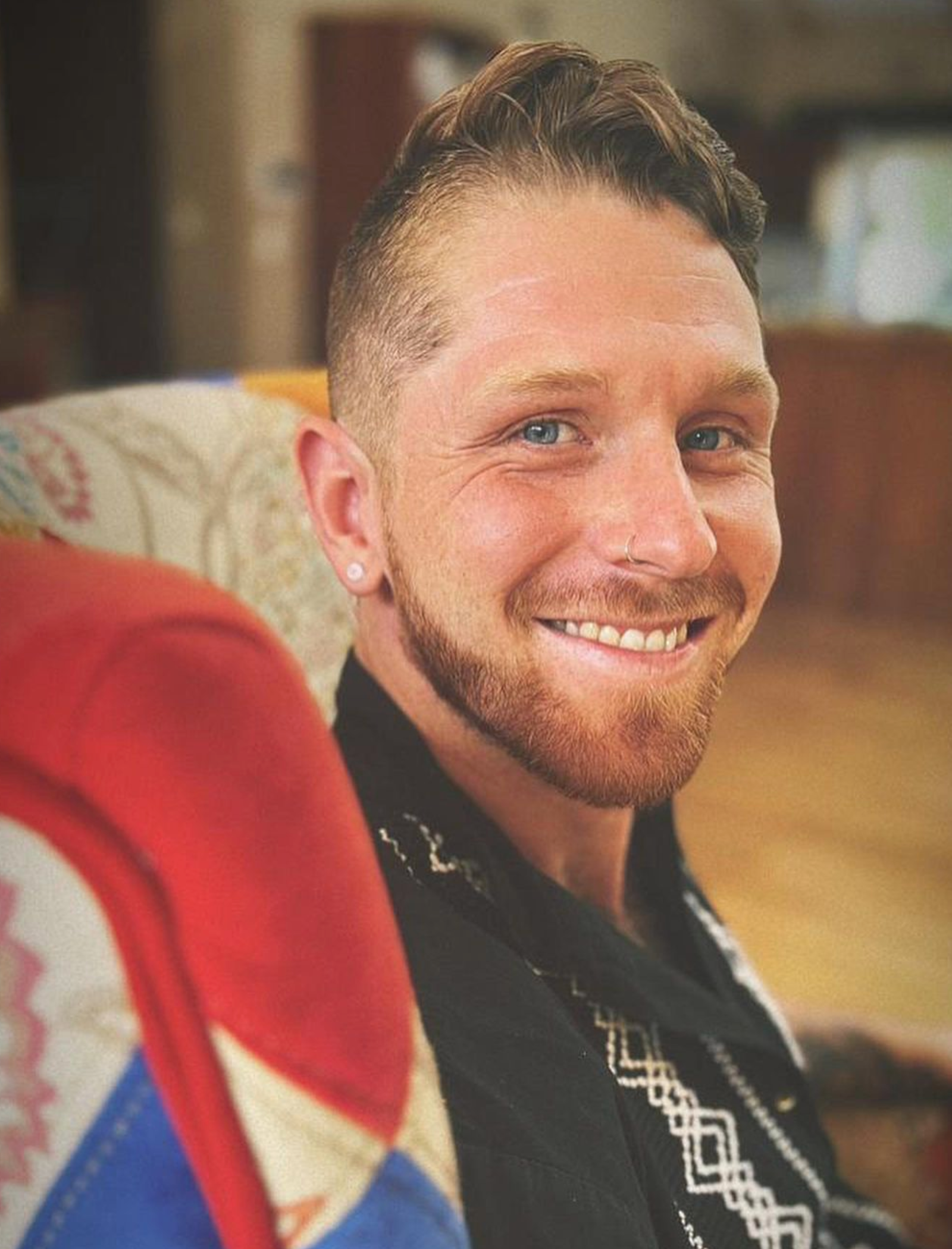 Smiling man with short hair and beard seated indoors in a casual setting