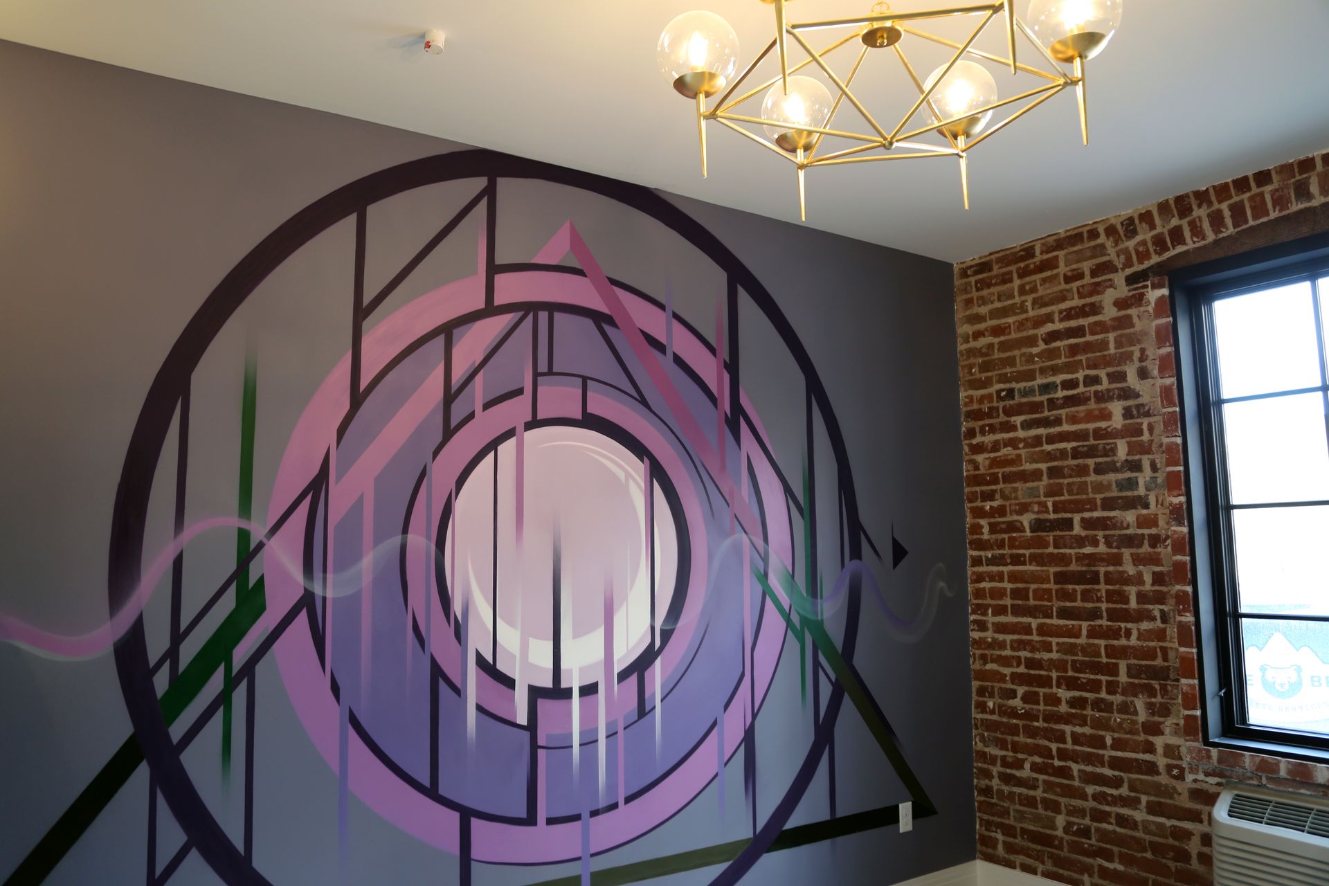 Abstract purple and black geometric mural on an interior wall beside a brick wall and window