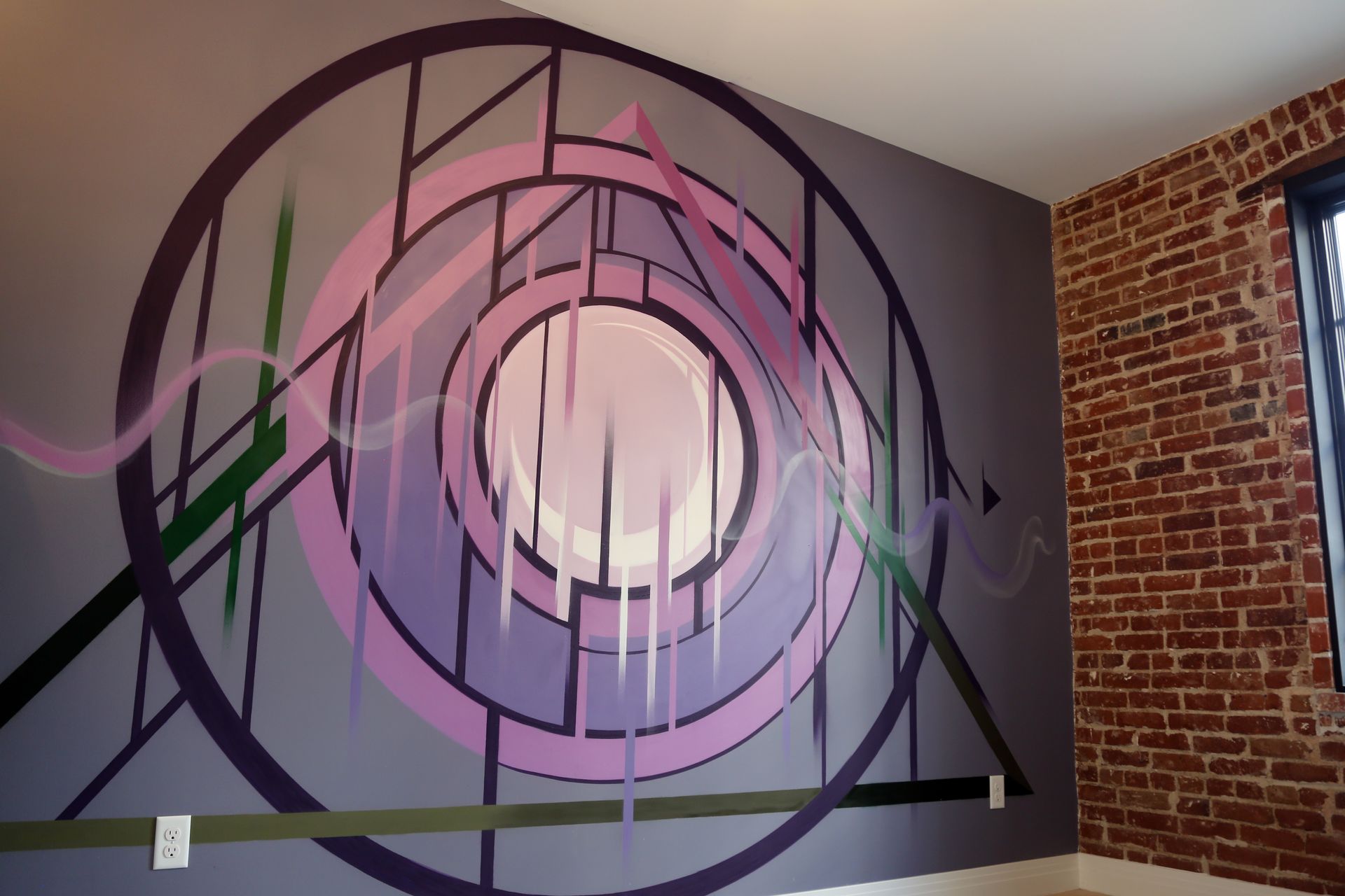 Abstract mural with pink and purple geometric swirls on a gray wall beside exposed brick.