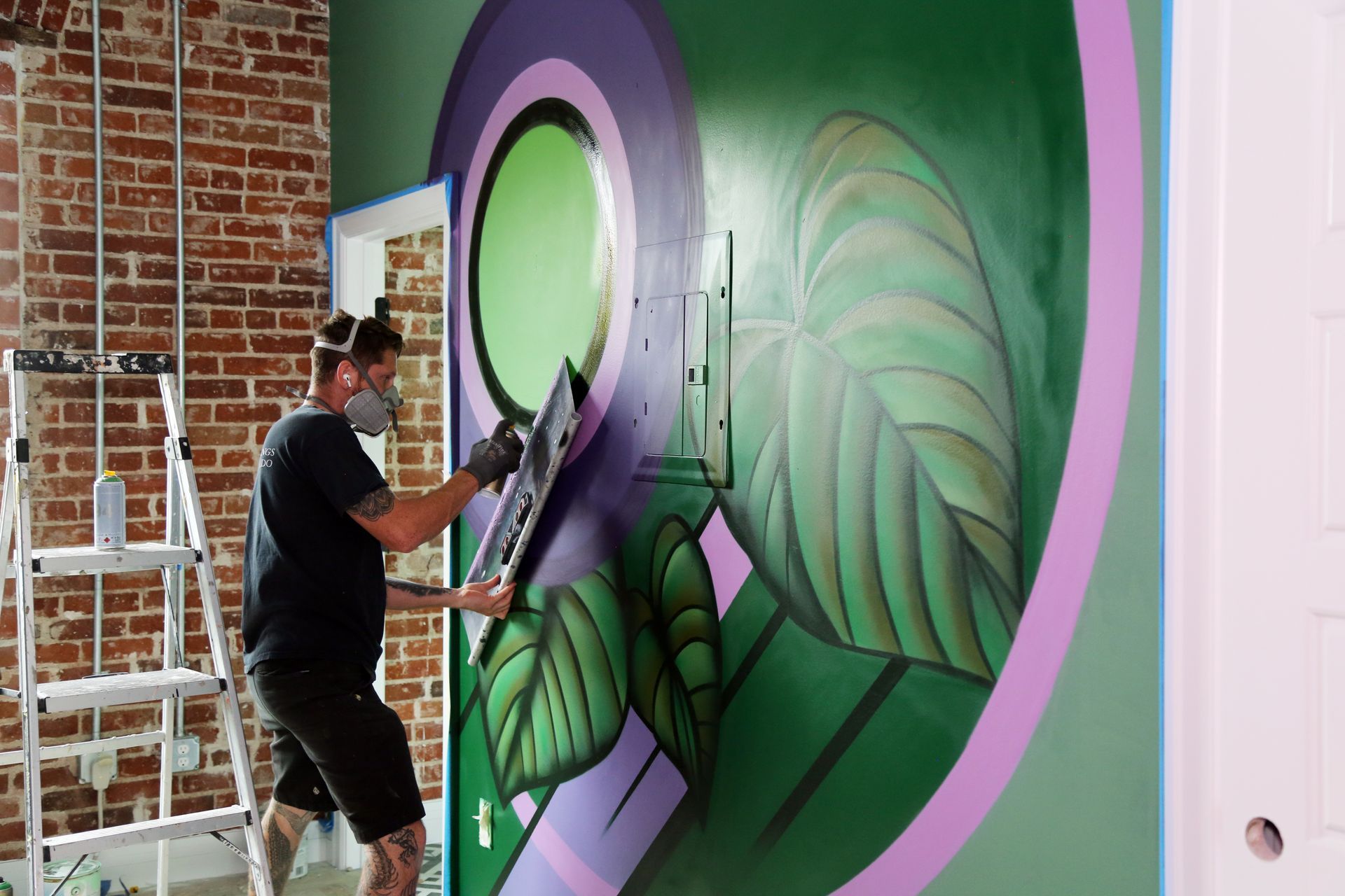 Artist painting a large green and purple mural on an indoor wall