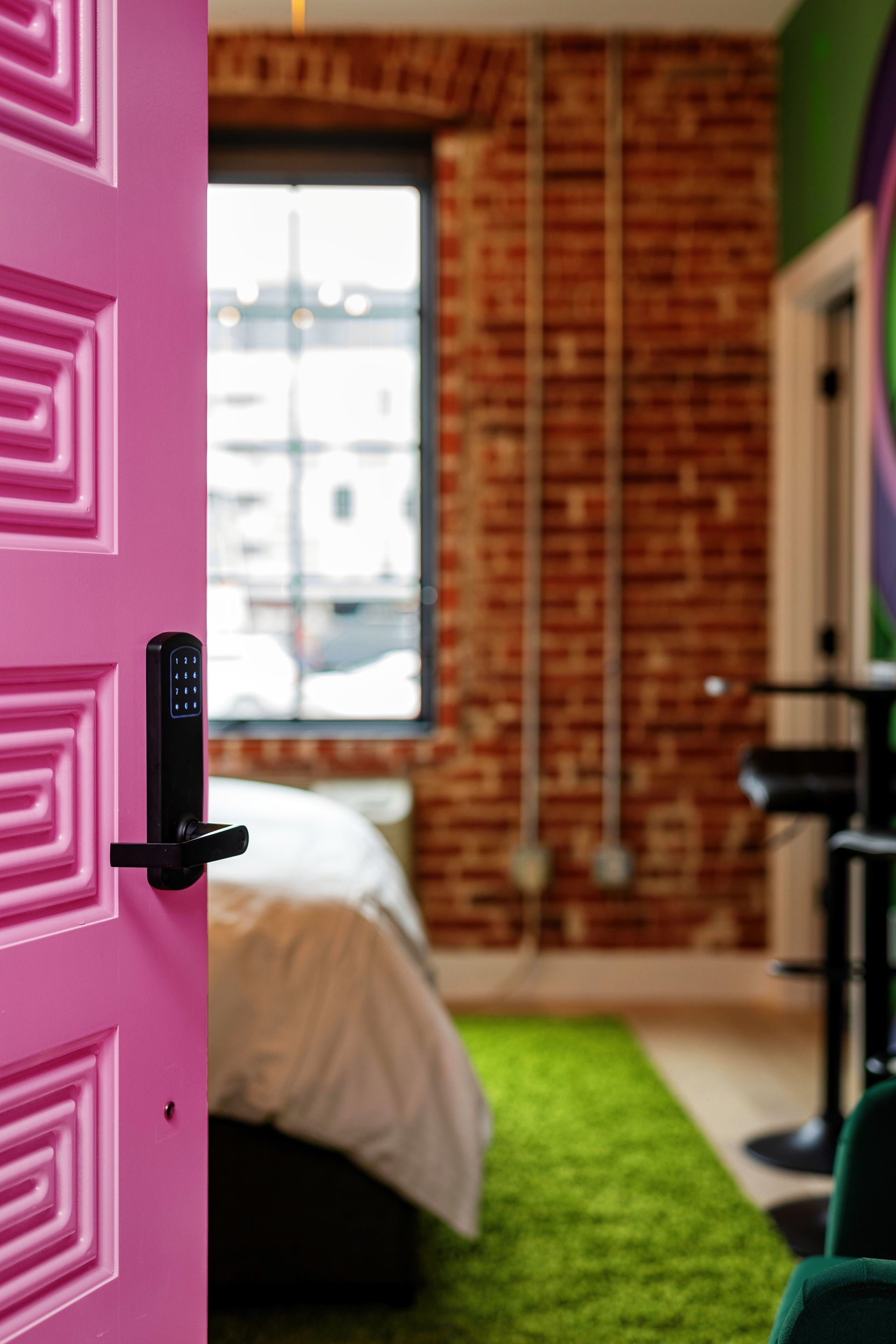 Open pink door to a bedroom with brick wall, green rug, and a window.