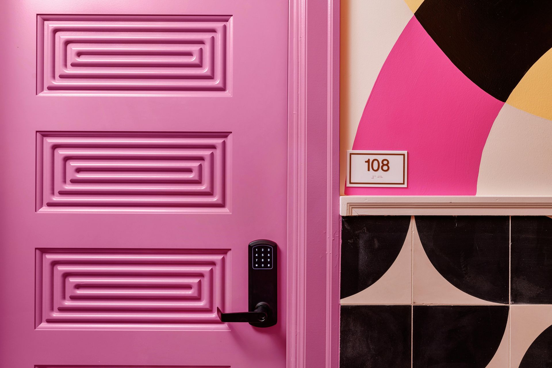 Pink door beside a geometric black, white, and pink wall with the number 108
